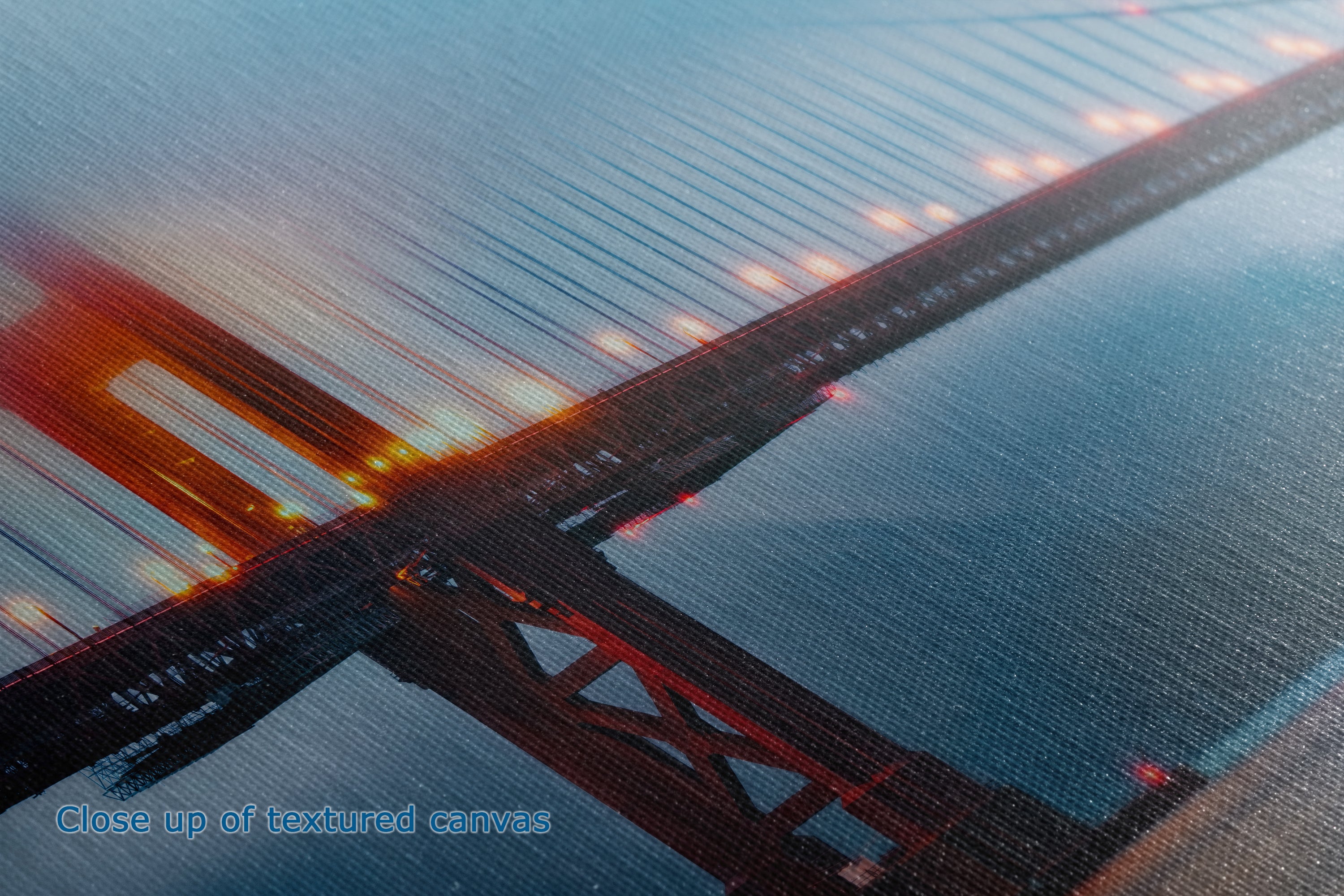A close-up of a printed or textured surface featuring a view of the Golden Gate Bridge over water at dusk, with warm orange-red lights and blue-gray sky and water tones.