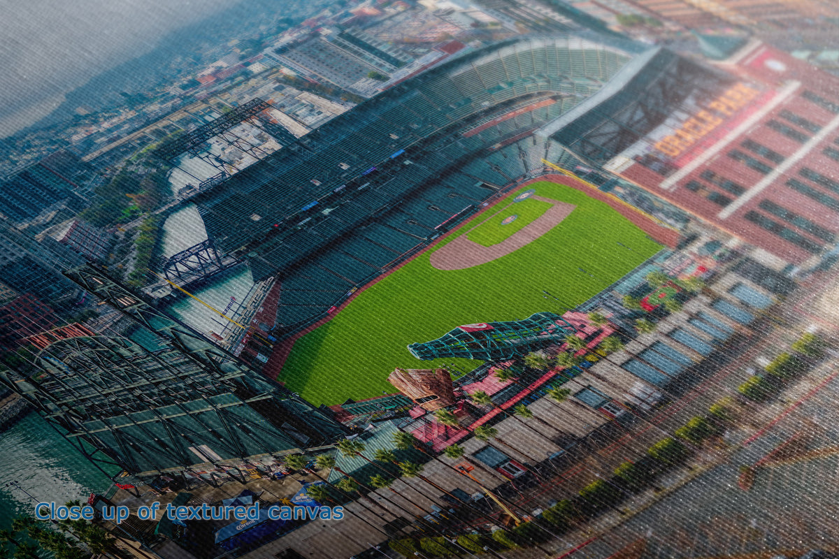 A close-up of the texture and detail of a canvas wall art print showing an aerial view of a baseball stadium with a green field, surrounding urban buildings, and a blurred overlay effect. Text at the bottom reads 'Close up of unedited canvas'.