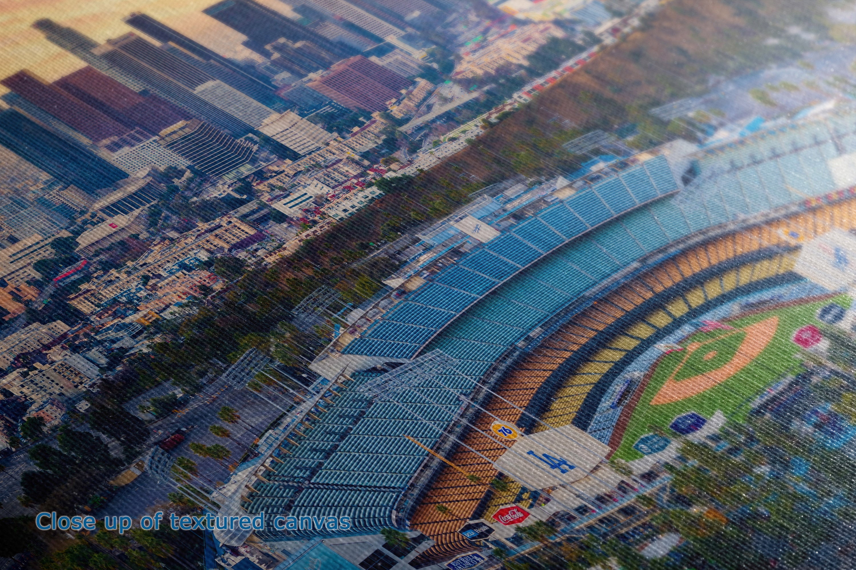 Aerial close-up view of a stadium with curved blue seating, green field, and surrounding city buildings at sunset.