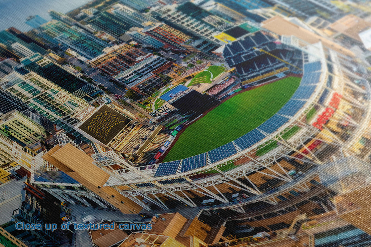 A close-up of the detail and texture of a canvas print depicting an aerial view of a stadium surrounded by dense urban buildings, with a blue text overlay in the bottom-left corner reading 'Close up of textured canvas'.