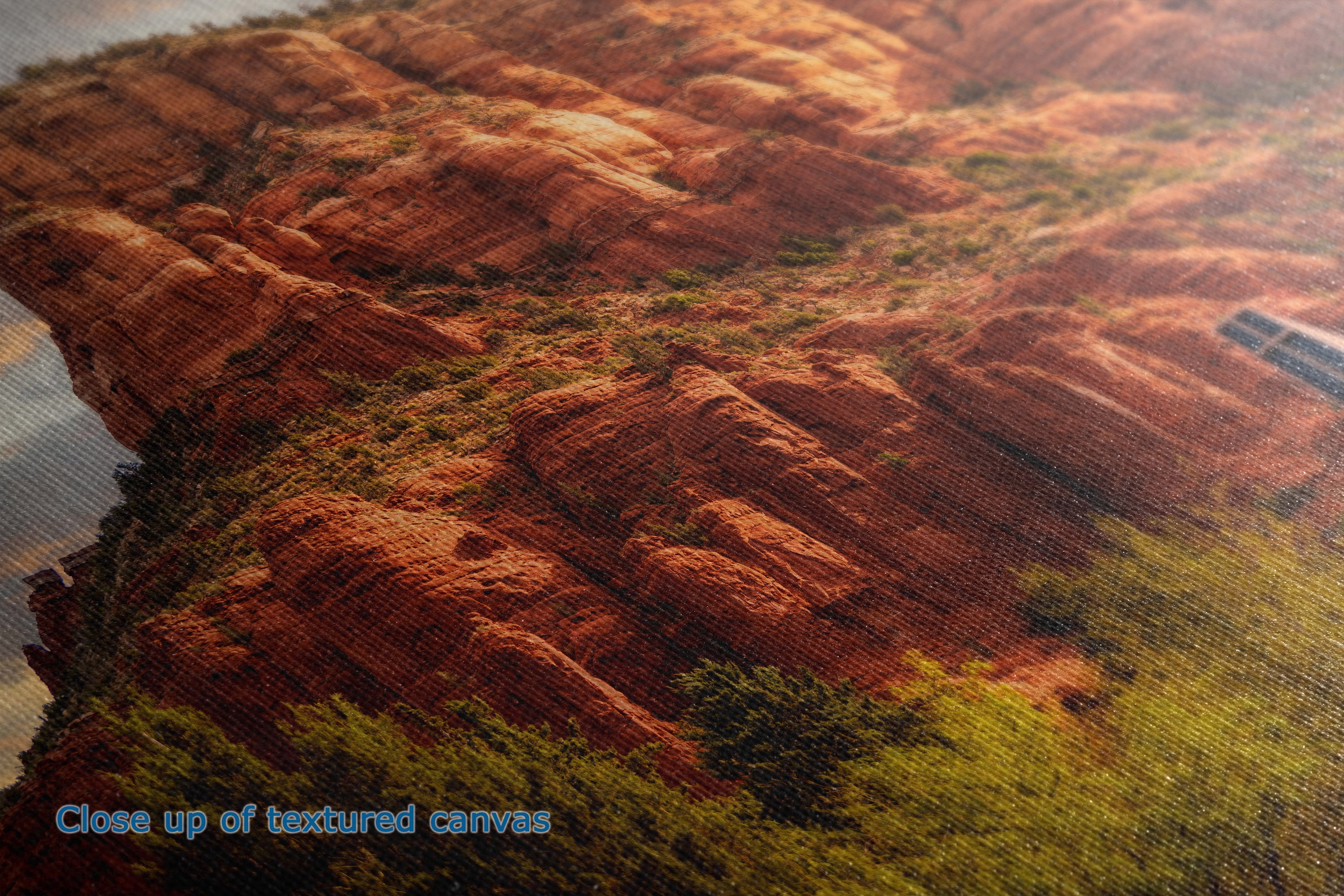 Close-up of the detail and texture of a canvas print depicting a desert canyon landscape with reddish-brown rock formations and green vegetation.