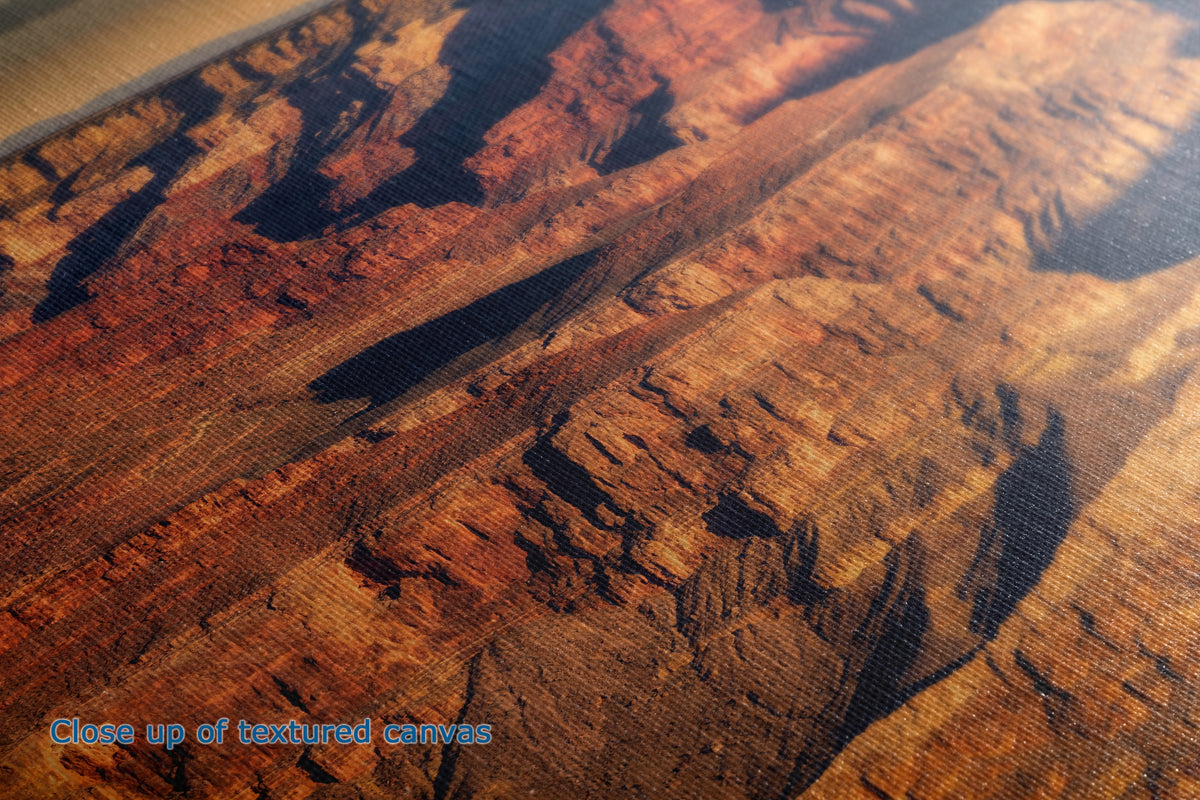 Close-up of a textured canvas print depicting a canyon landscape with warm orange, brown, and red rock formations under a golden light.