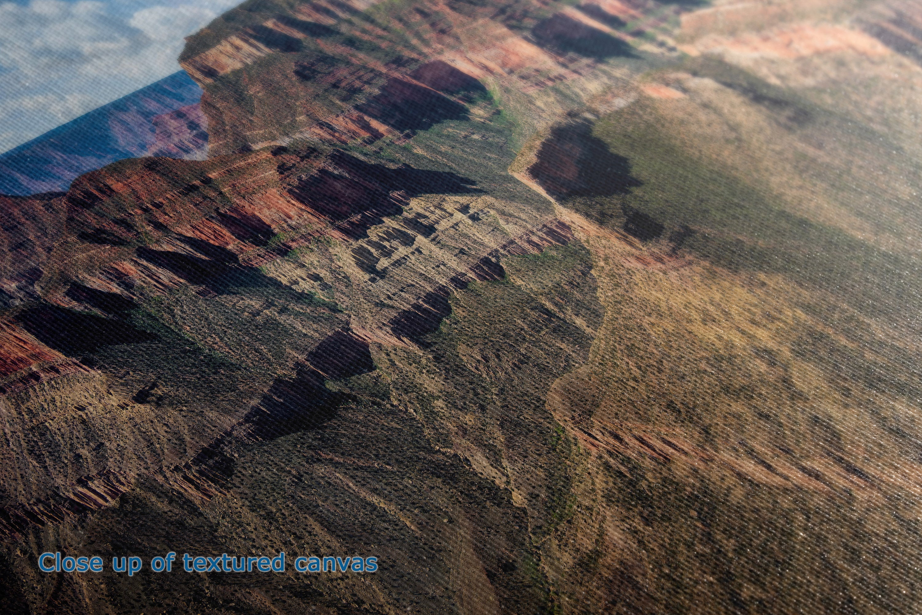 Close-up of a textured canvas print depicting a canyon landscape with layered red, brown, and green rock formations under a blue sky.