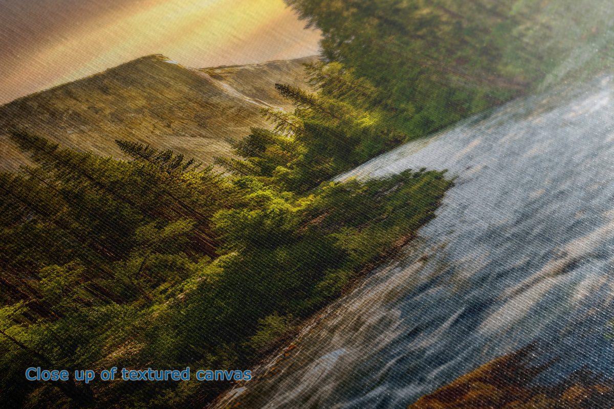 A close-up of the detail and texture of a canvas wall art print showing a forested hillside beside a flowing river under warm golden light.