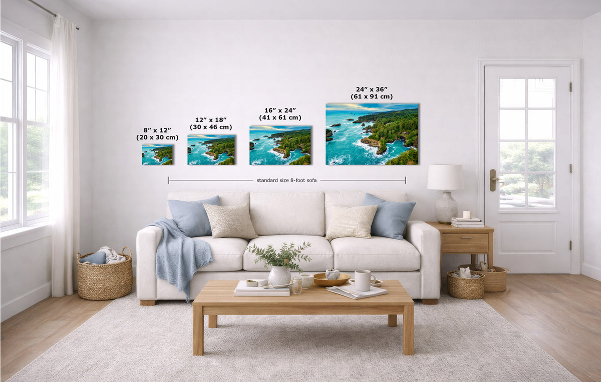 A staged living room shows a set of four coastal landscape wall art prints above a white sofa. The prints depict blue water, green shoreline, and tan rocks, with size labels overlaid in inches and centimeters.