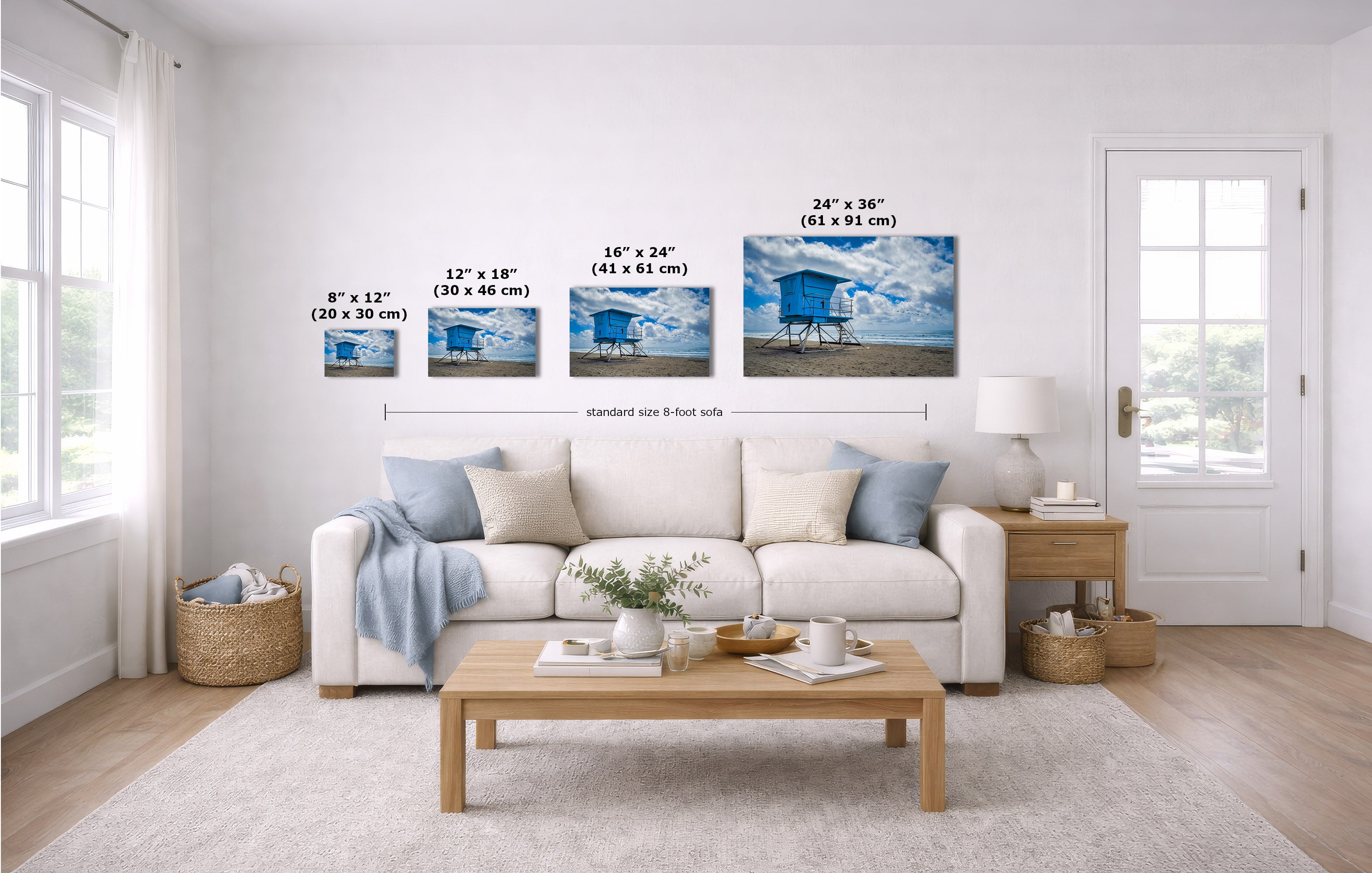 A staged living room shows a set of four wall art prints above a white sofa. The prints depict blue beach cabanas under a cloudy sky, with size labels overlaid in inches and centimeters.