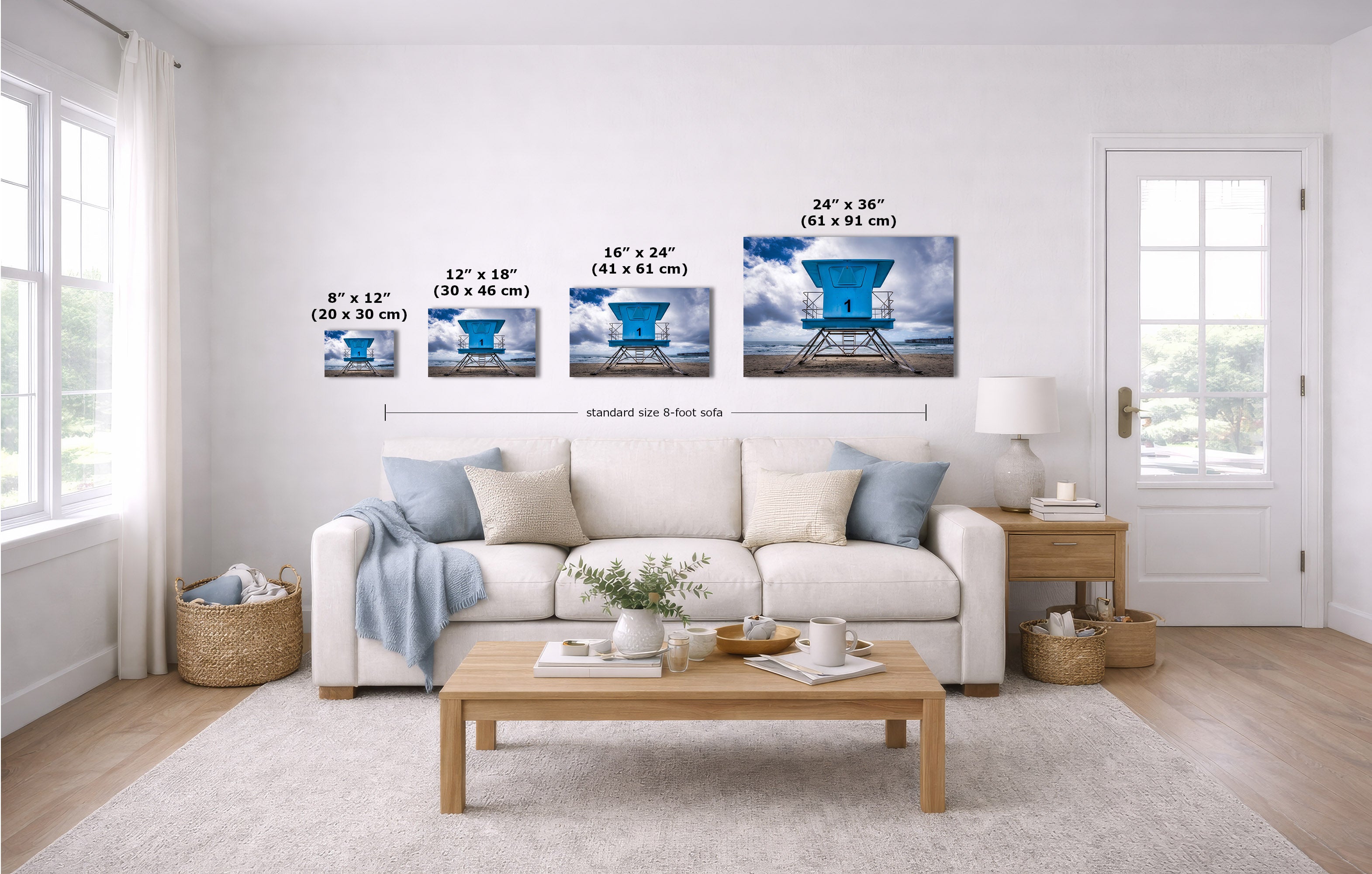 A staged living room shows a set of four wall art prints depicting a blue lifeguard tower scene, with size labels overlaid above each frame. The room includes a white sofa, wood coffee table, rug, and windows.