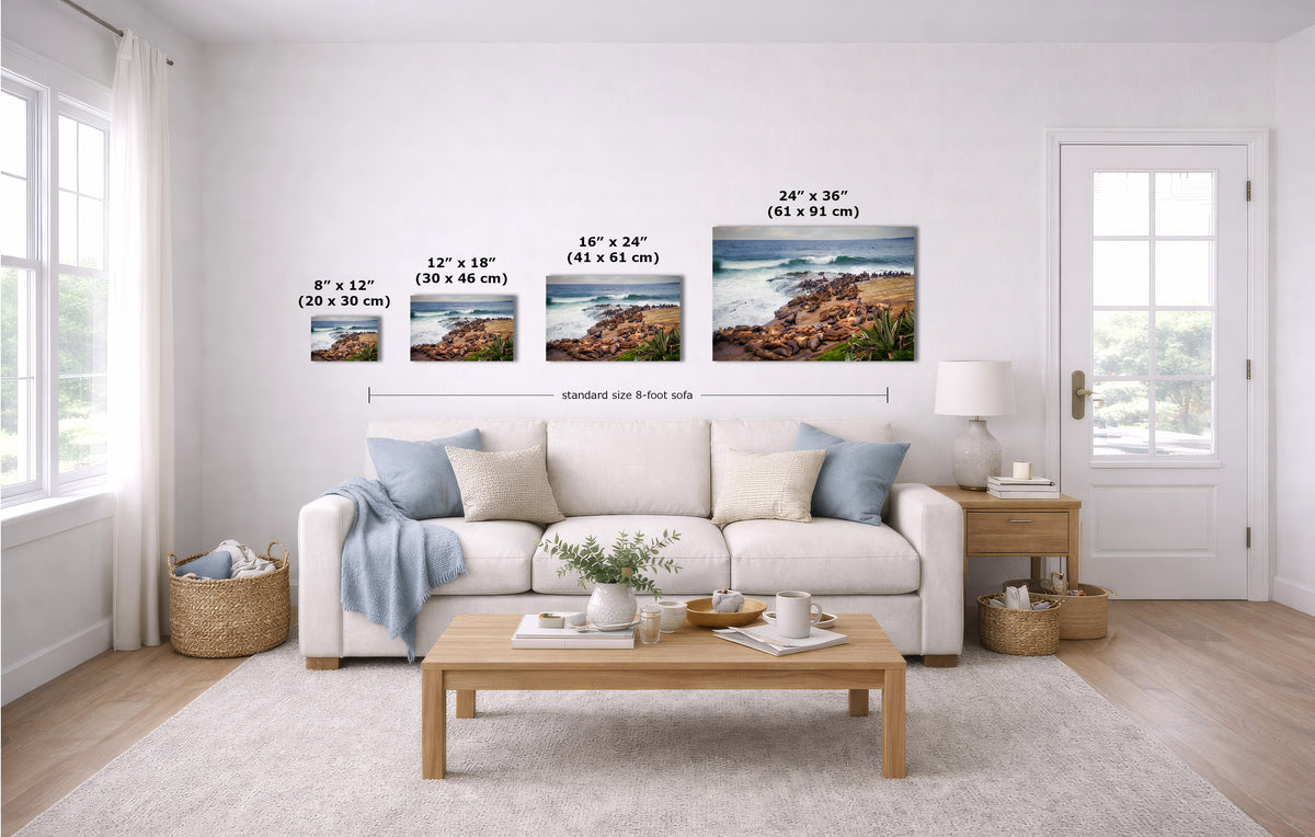A staged living room with a white sofa, coffee table, and wall-mounted framed coastal landscape prints. Black measurement labels and arrows indicate the width of each print and a standard 8-foot wall spacing.
