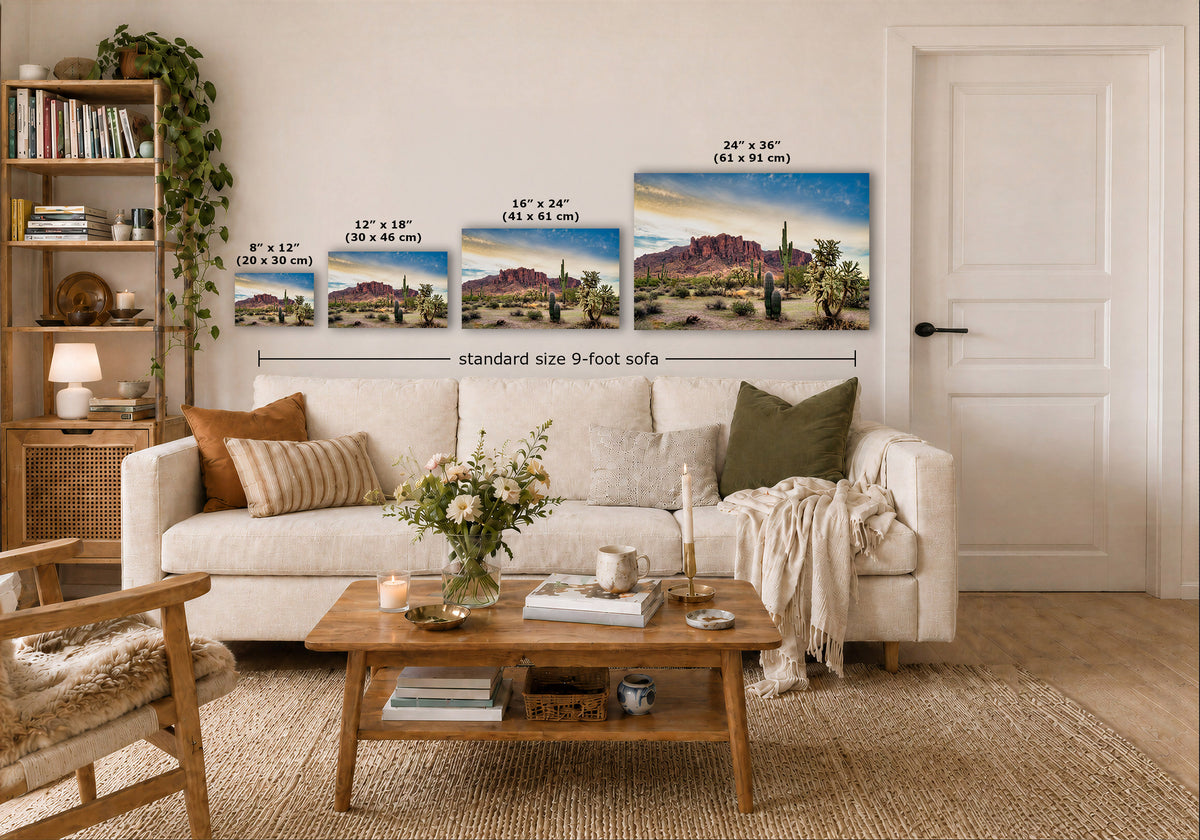 A staged living room shows a white sofa with pillows, a wooden coffee table, shelving, and a door, with three desert landscape wall art prints above the sofa. Small size labels and the text 'standard size 9-foot sofa' appear over the artwork.