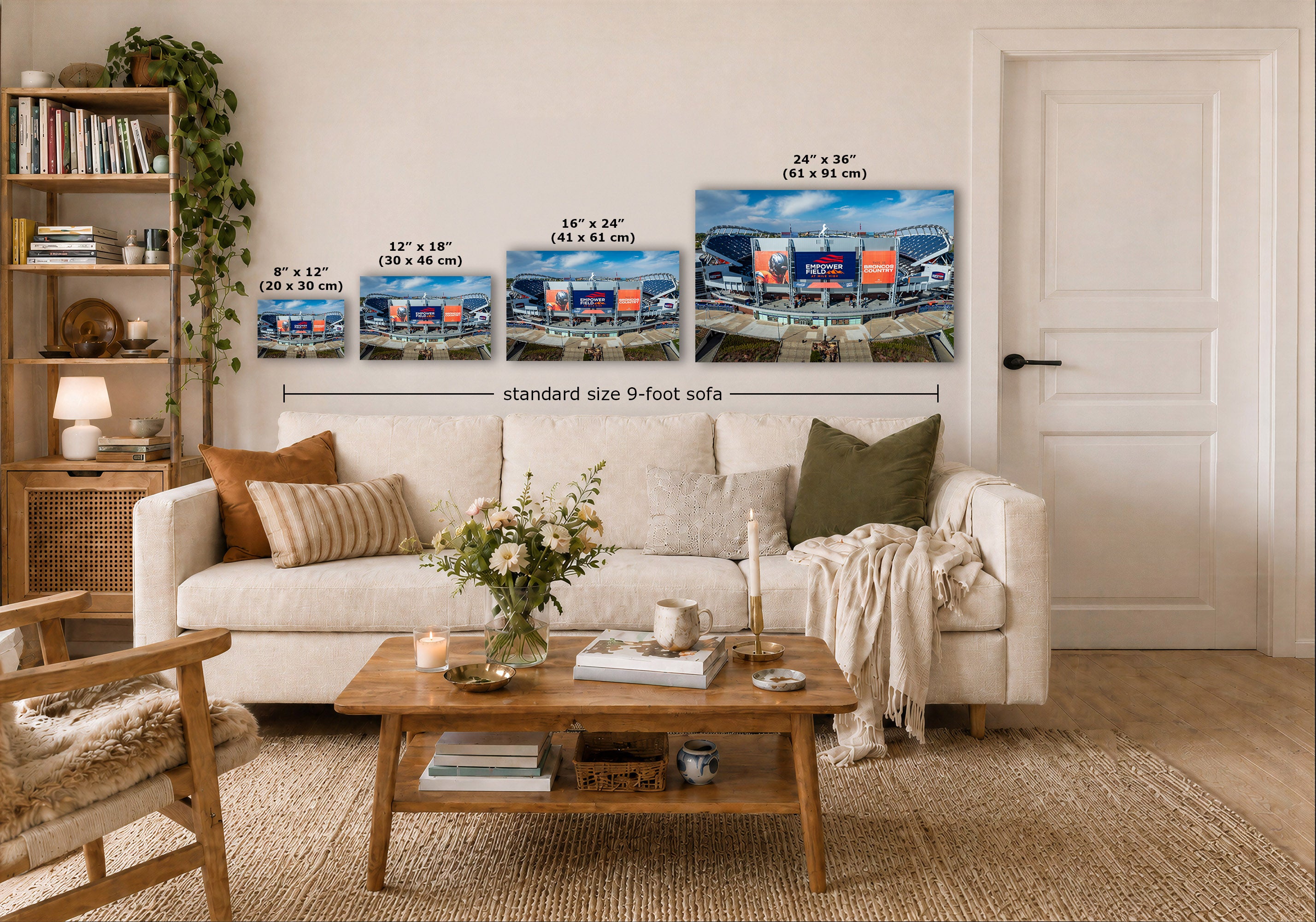 A staged living room shows a white sofa with pillows, a wooden coffee table, shelving, and a door, with wall art above the couch displaying stadium scenes and size text labels. The scene appears to be a room mockup demonstrating wall art in context rather than a clean isolated product shot.