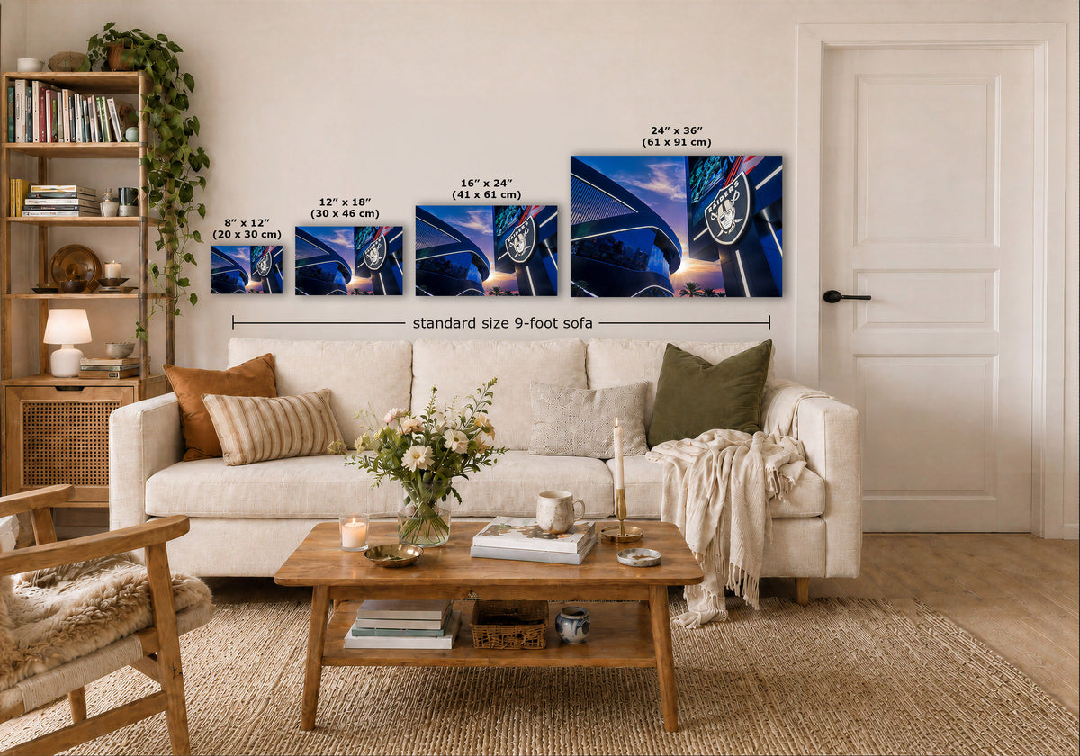 A styled living room showing four framed wall art prints above a white sofa, with size labels indicating 8 x 12, 12 x 18, 16 x 24, and 24 x 36 inches. The prints depict a dark blue and black exterior stadium scene of the Raiders stadium in Las Vegas, Nevada.
