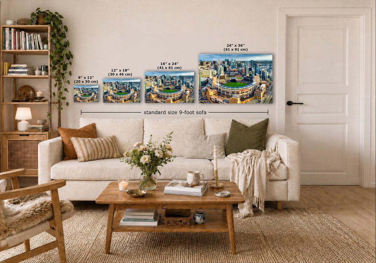 Four wall art prints showing a city skyline and stadium scene are displayed above a white sofa in a styled living room. White dimension labels and text indicate sizes such as 8 x 12, 12 x 18, 16 x 24, and 24 x 36, with a note reading standard size 9-foot sofa.