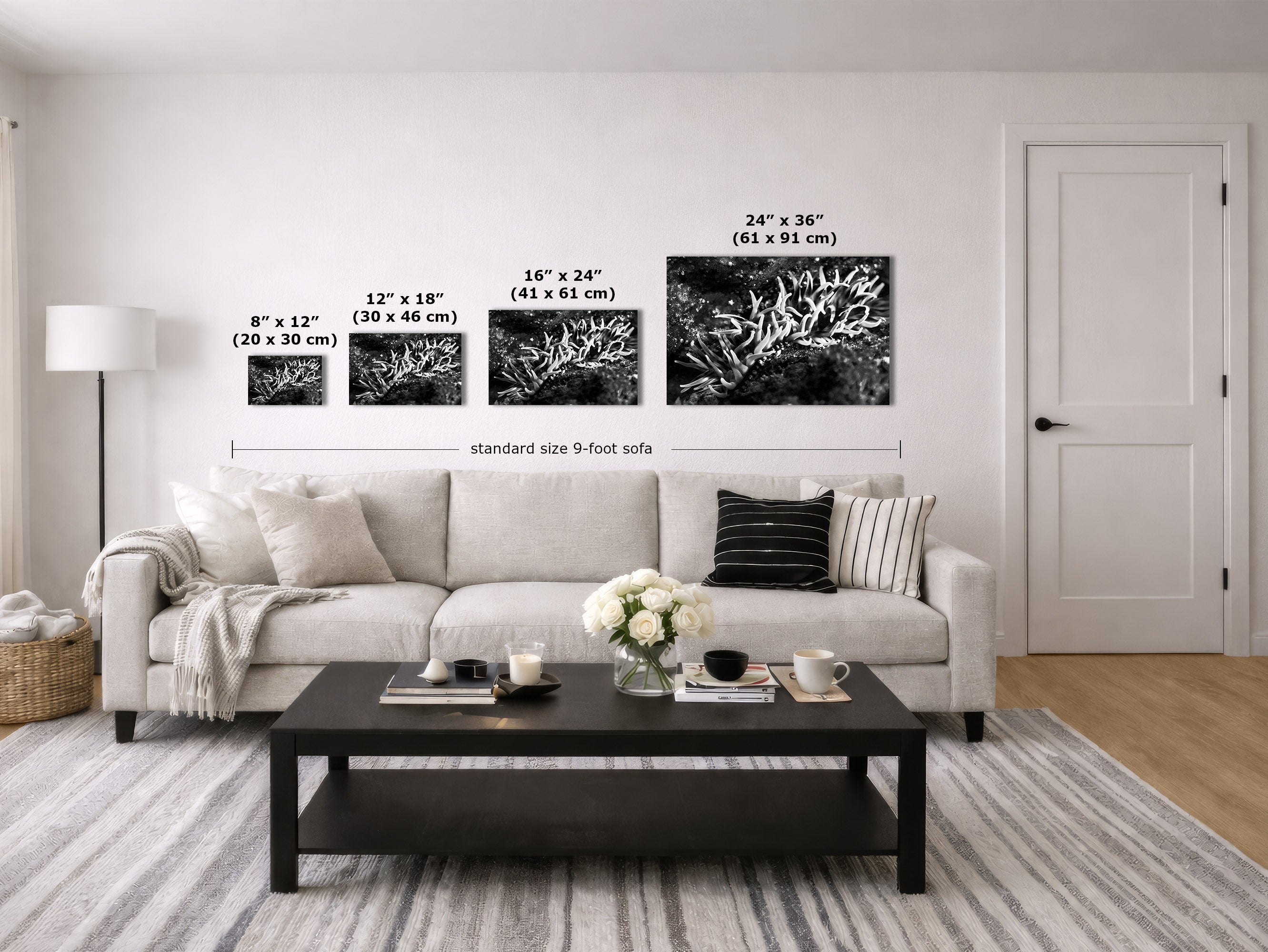 A staged living room showing four black-and-white wall art prints in different sizes mounted above a light sofa. White text labels indicate the dimensions of each print and a standard 9-foot sofa width below.