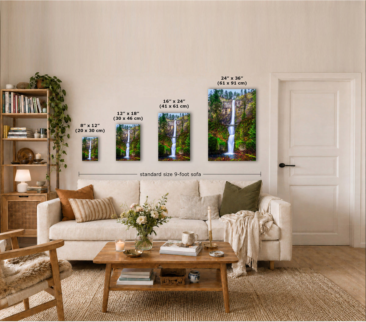 A staged living room showing four vertical wall art prints of waterfalls in forest canopies, each labeled with different dimensions. The prints are displayed above a cream sofa, with a coffee table, books, and a door in the room.