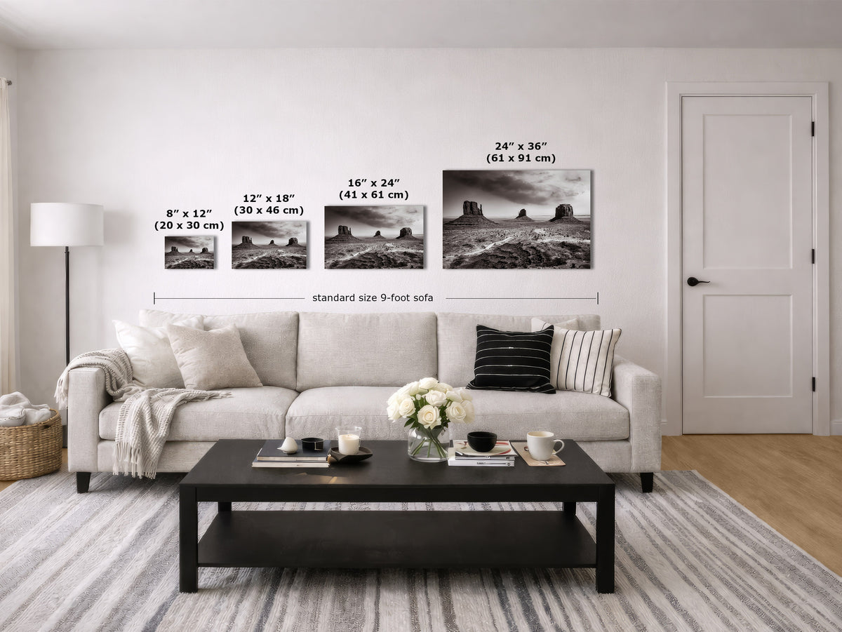 A staged living room showing a set of four black-and-white landscape wall art prints above a light sofa, with size labels and measurements for each print and a total sofa width reference.