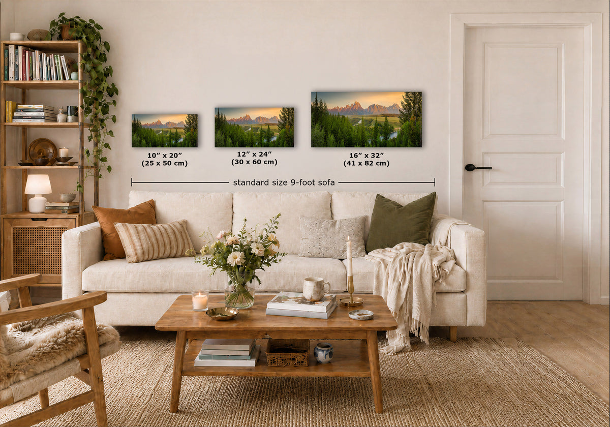 Three framed mountain landscape prints are displayed above a white sofa in a styled living room. Each print shows a different sunset scene with green trees, blue water, and warm golden light.