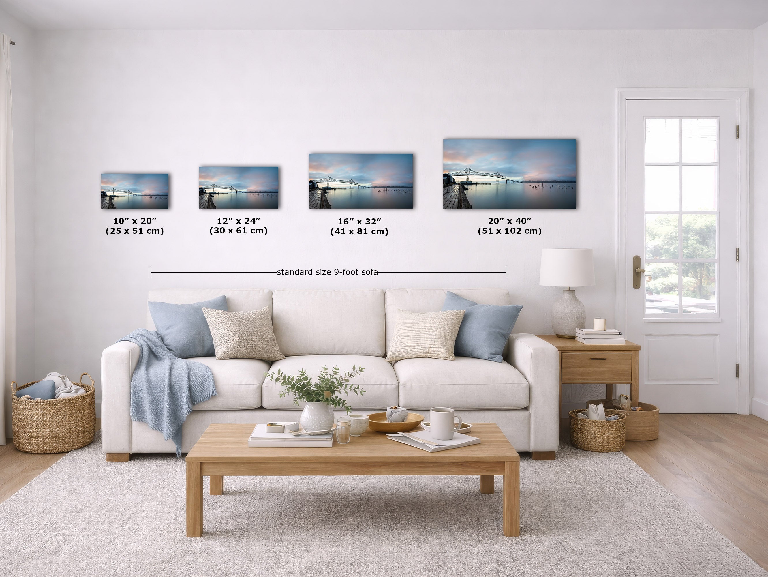 A staged living room with a white sofa, coffee table, and wall art showing four horizontal landscape prints with size labels beneath them. The room is bright and neutral, and the wall art appears to be the product being demonstrated in context.