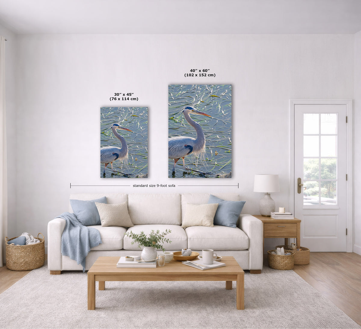 A staged living room shows two framed wall art prints above a sofa. The prints depict a blue heron in a marsh scene.