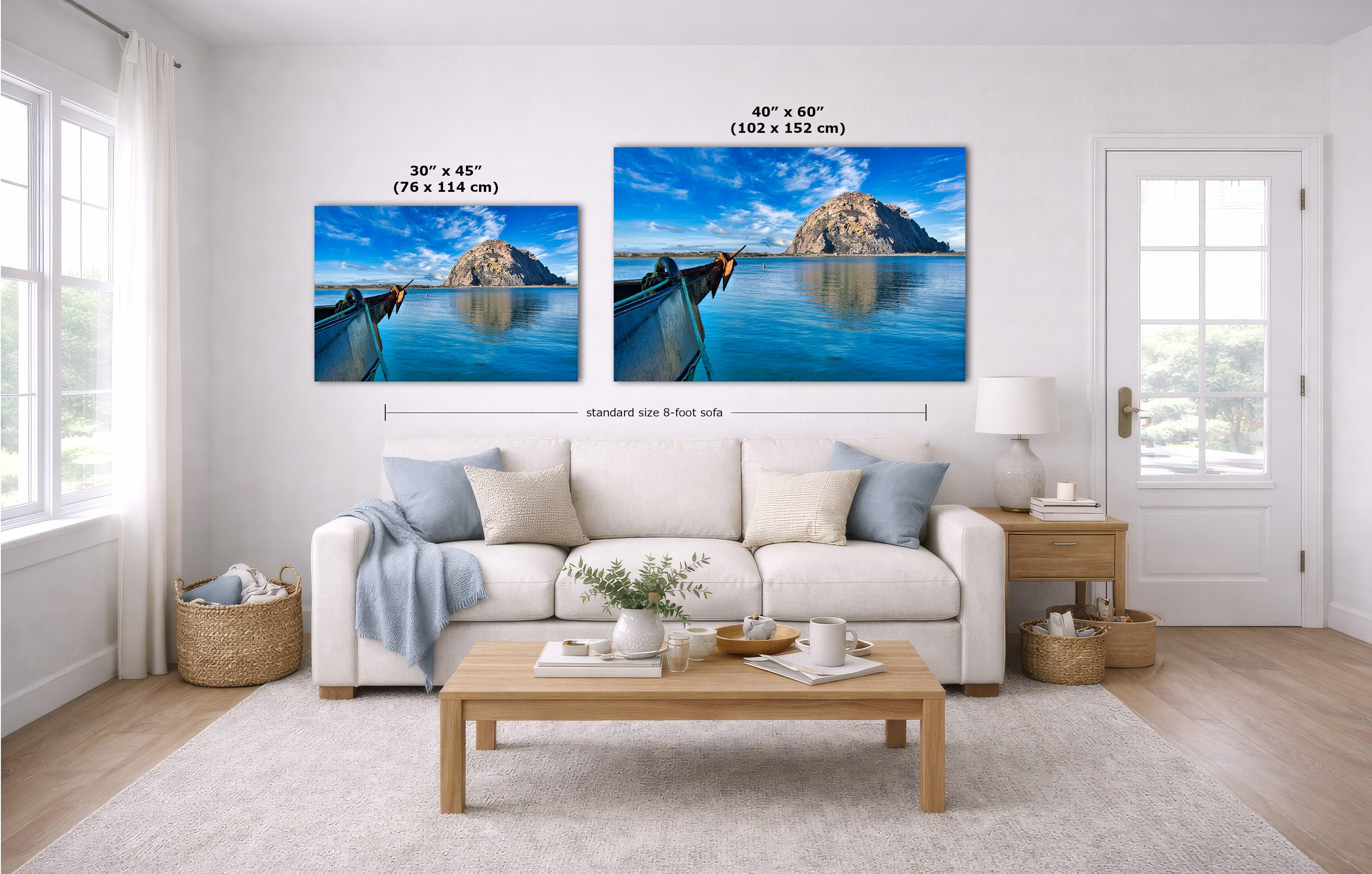 A staged living room with a white sofa, coffee table, and wall art showing two landscape prints above the couch. The prints depict a blue water scene with a rocky island and long boats.