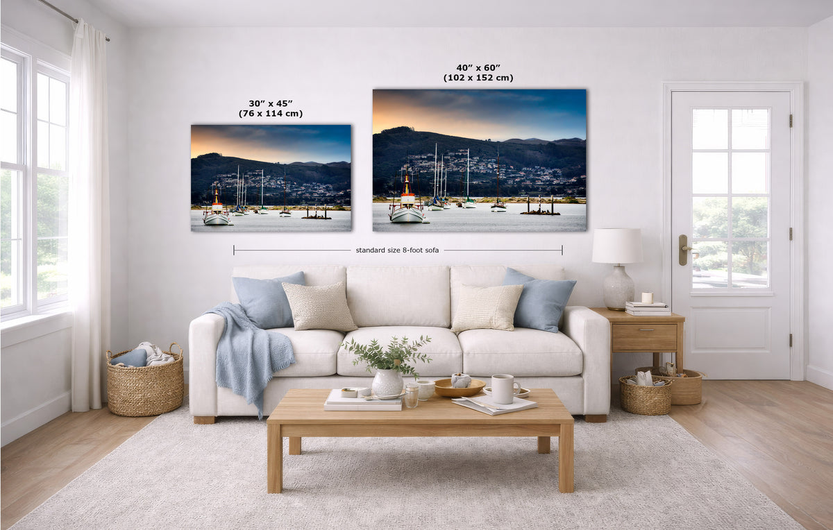 A staged living room shows two wall art prints above a white sofa. The prints depict a coastal harbor sunset scene with boats and mountains.