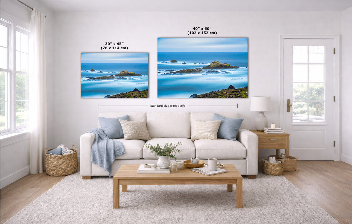A staged living room shows two coastal ocean wall art prints above a white sofa. The left print is labeled 30 x 45 inches, and the right print is labeled 40 x 60 inches.