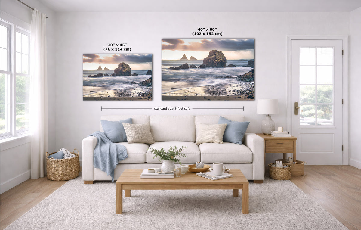 A styled living room showing two coastal landscape wall art prints above a white sofa, with size labels and dimension lines indicating 30 x 45 inches and 40 x 60 inches. The room includes a light wood coffee table, beige rug, side table, lamp, and windows.