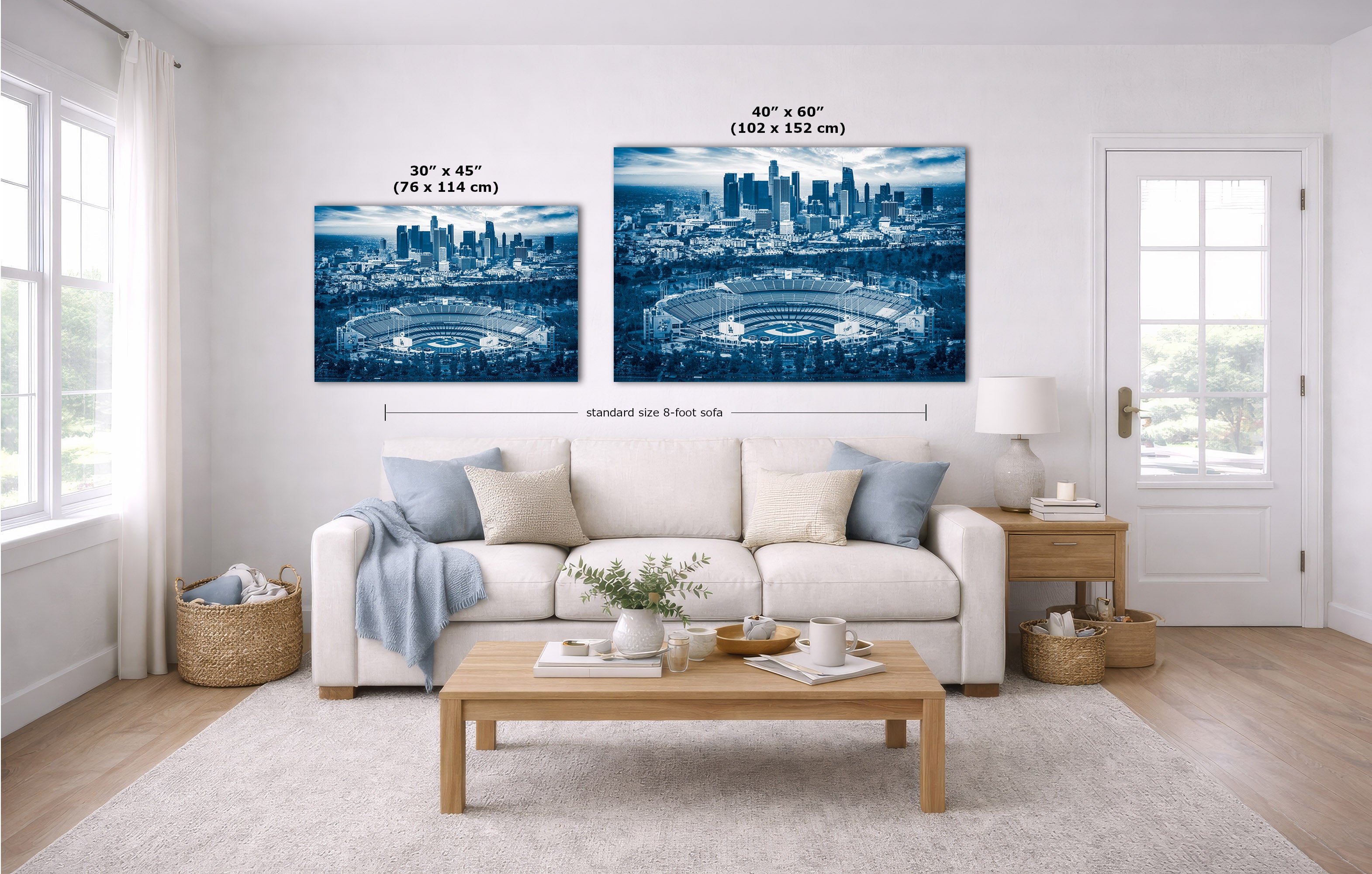 Two blue-toned city stadium wall art prints displayed above a white sofa in a bright living room, with size labels and dimension lines overlaid on the artwork.