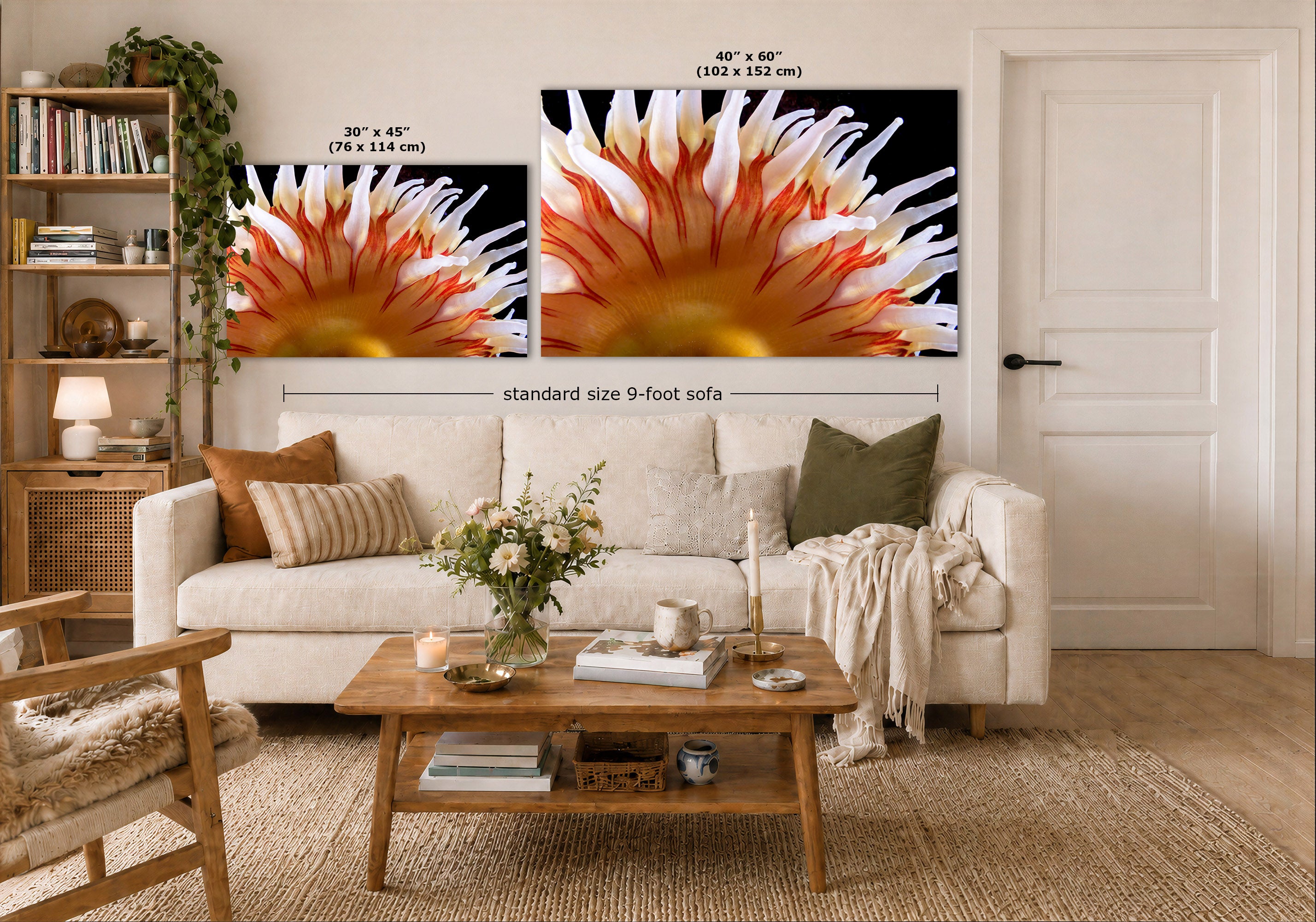 Two wall art prints showing close-up anemone scenes in black, orange, white, and red tones, displayed above a white sofa in a styled living room. Size labels and a dimension line indicate the print dimensions relative to a standard 9-foot sofa.