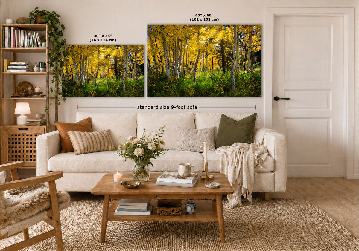 A styled living room showing two wall art prints above a white sofa. The prints depict a bright yellow autumn forest with tall trees and green undergrowth.