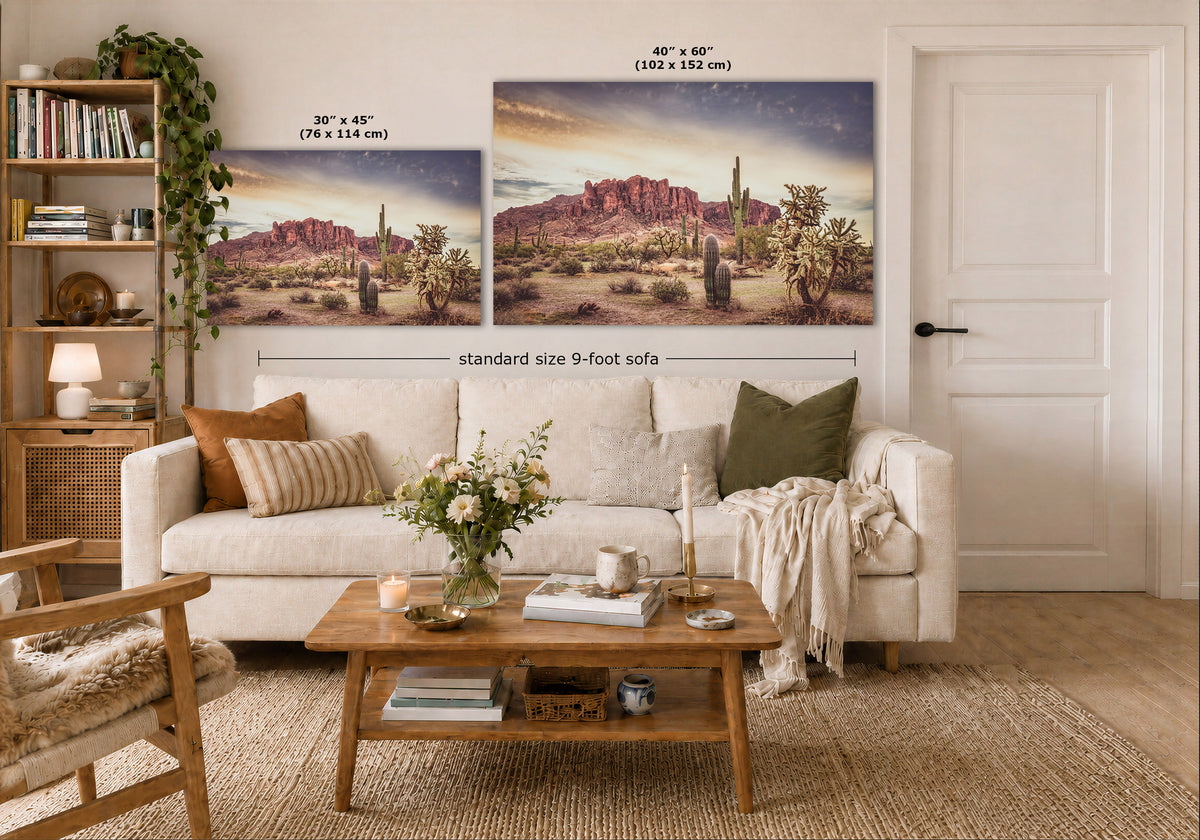 A styled living room showing two desert landscape wall art prints above a white sofa, with size labels overlaid: 30 x 45 inches for the smaller print and 40 x 60 inches for the larger print. The room includes a wooden coffee table, shelving, rug, and door.