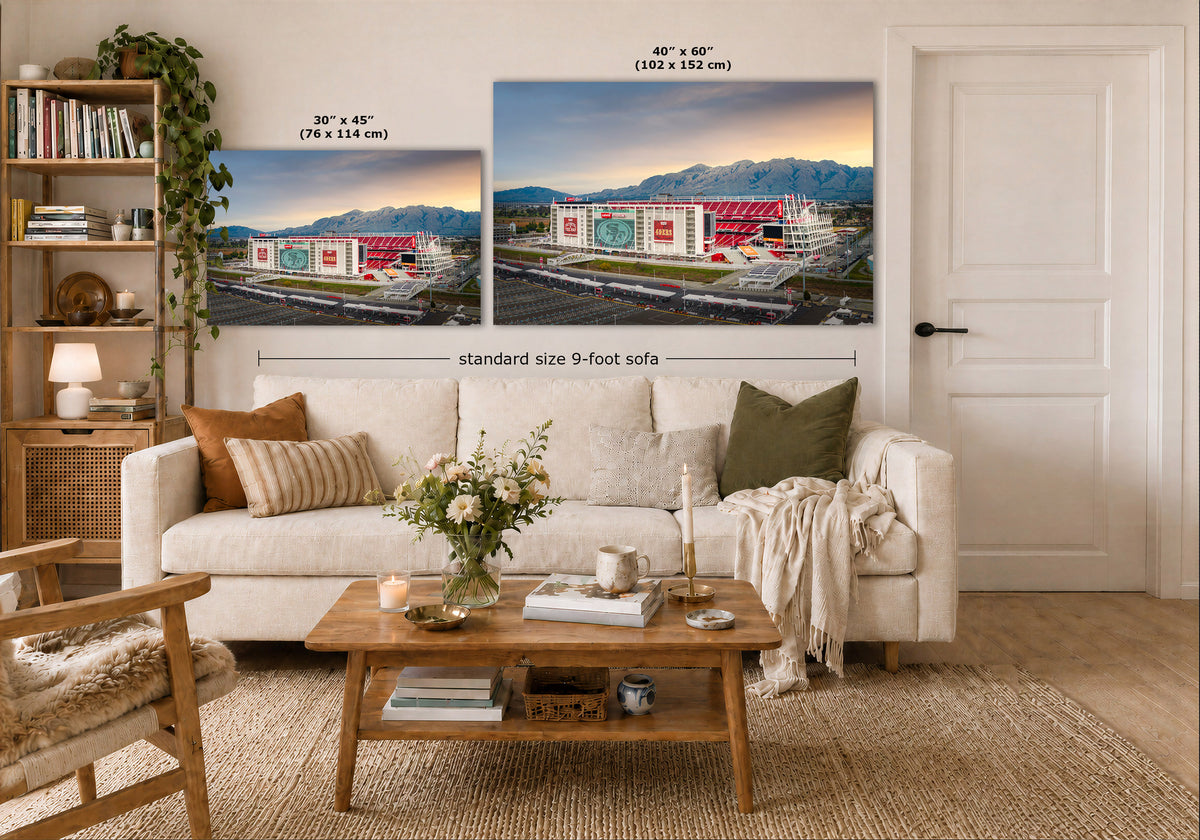A styled living room showing two wall art prints above a white sofa. The prints depict a stadium scene at sunset, with one smaller 30 x 45 inch print and one larger 40 x 60 inch print.