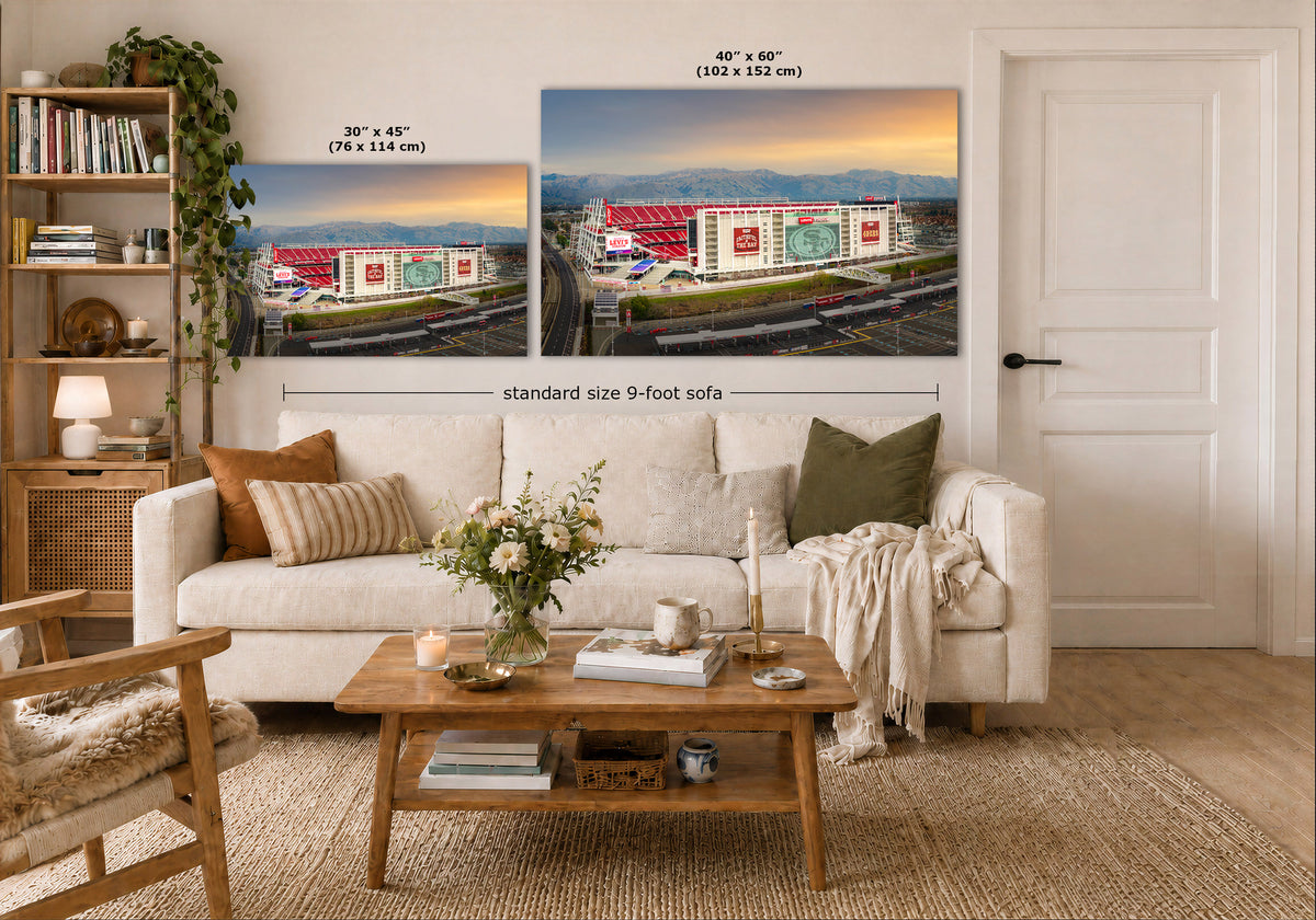 A styled living room showing two large wall art prints above a white sofa, with dimension labels indicating 40 x 60 inches and 30 x 45 inches sizes. The prints depict stadium scenes at sunset, and the room includes a coffee table, books, chair, and door.