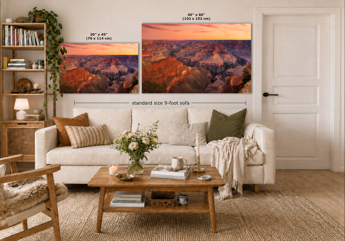 A staged living room shows two wall art prints above a white sofa. The prints depict a canyon landscape at sunset in warm orange, pink, purple, and brown tones.