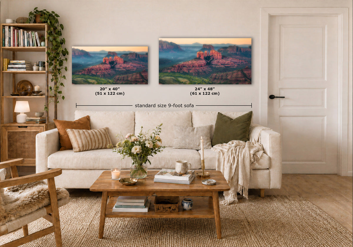 Two landscape art prints of a desert canyon at sunset are displayed on a beige wall above a white sofa in a styled living room. Black dimension lines and text indicate the sizes: 20" x 40" (51 x 122 cm) and 24" x 48" (61 x 122 cm), labeled as standard size 9-foot sofa.