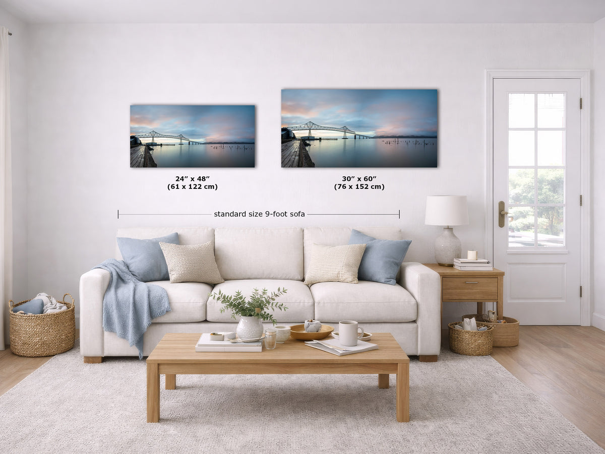 Two framed wall art prints showing a pier over calm water at sunset, displayed above a white sofa in a bright living room. Black text labels indicate the sizes 24" x 48" and 30" x 60" with a note reading standard size 9-foot sofa.