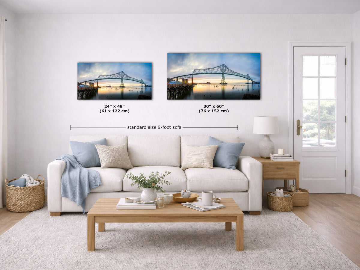 Two canvas wall art prints showing a bridge over water, displayed above a white sofa in a bright living room. Black dimension lines and text indicate the sizes of the two prints: 24" x 48" (61 x 122 cm) and 30" x 60" (76 x 152 cm), with 'standard size 9-foot sofa' written below.
