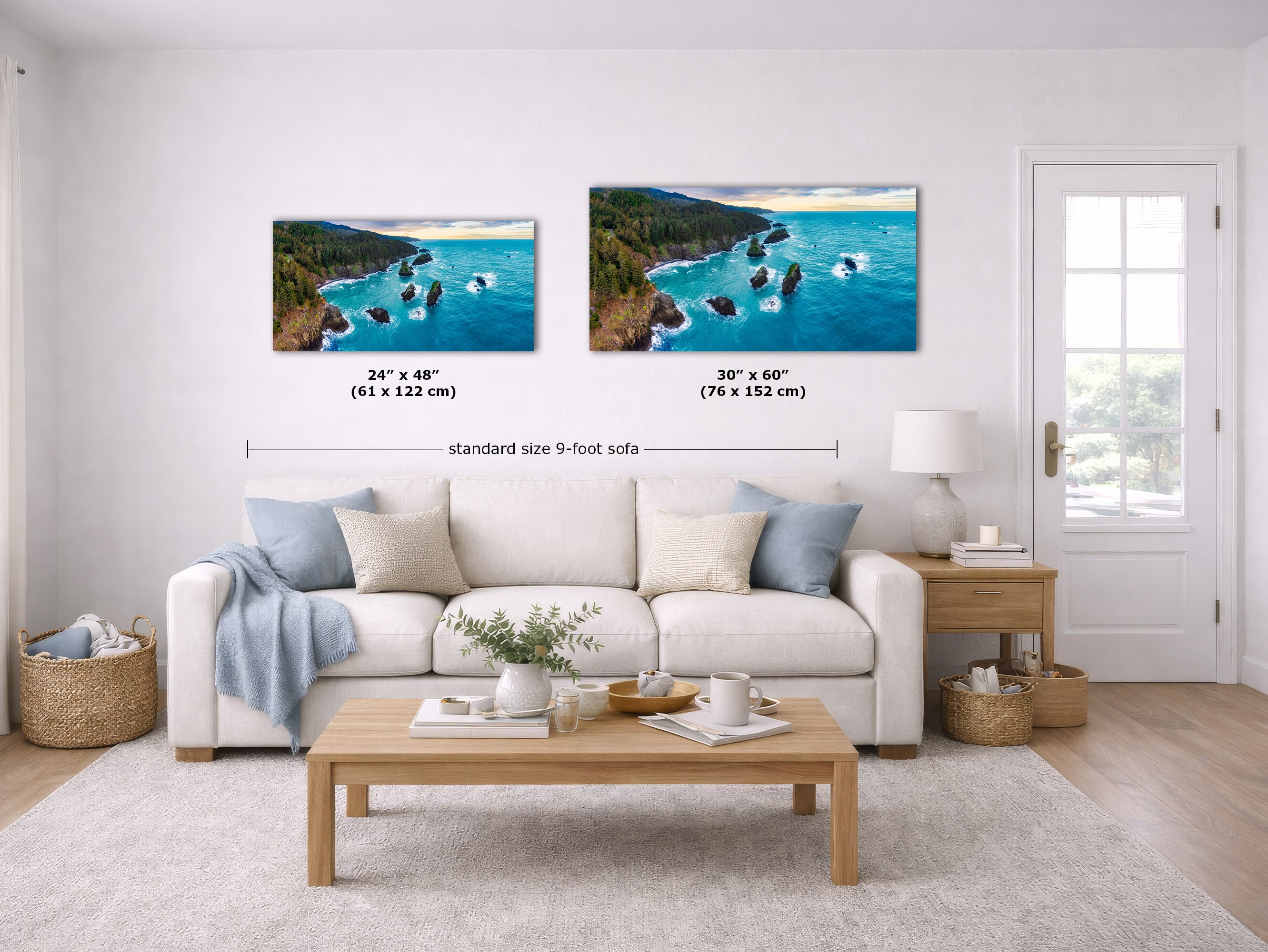 A staged living room with a white sofa, wooden coffee table, and wall art showing two coastal landscape prints. The prints depict bright blue water, dark green cliffs, and rocky shores.