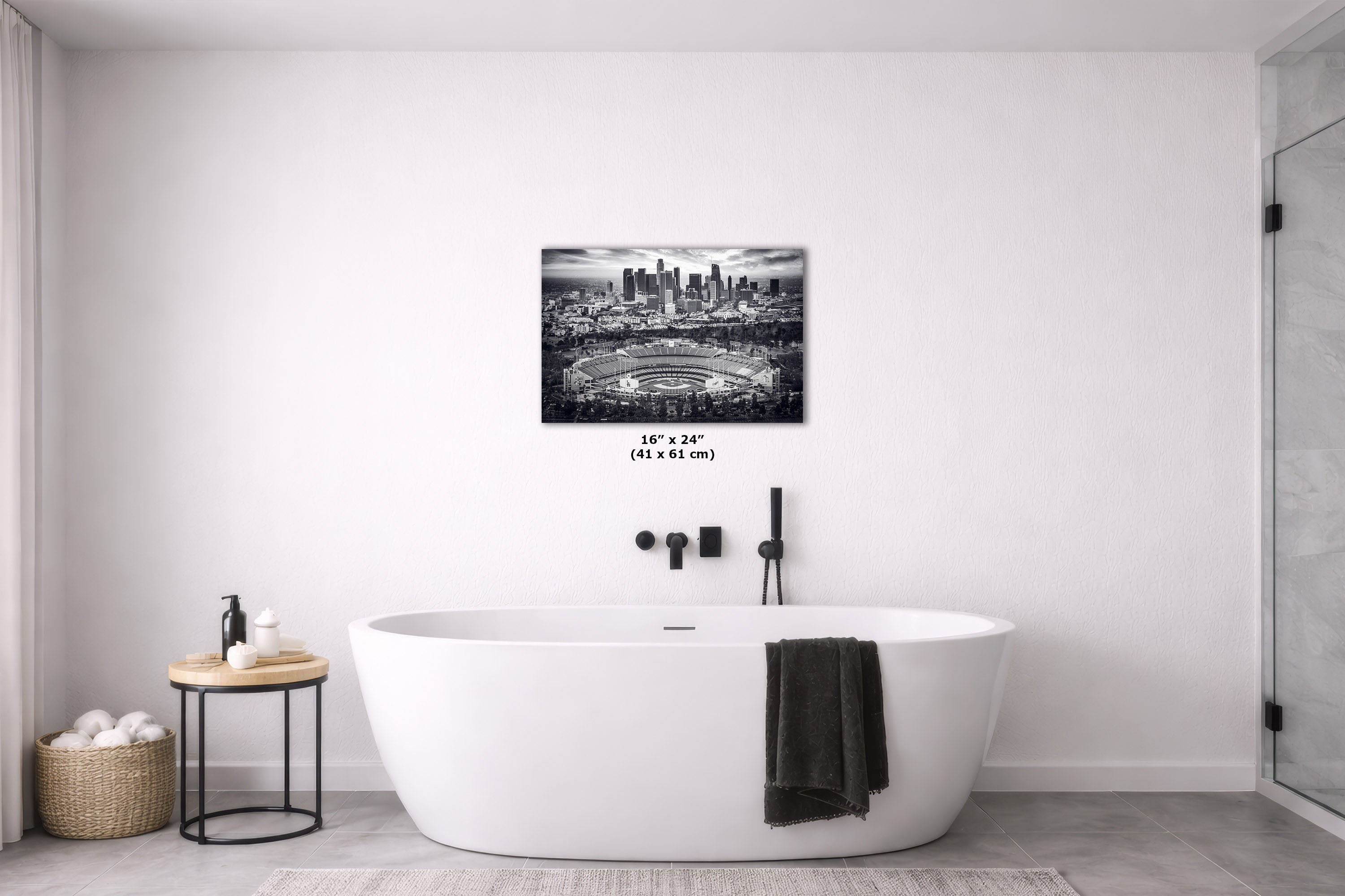 A black-and-white Los Angeles skyline canvas print showing Dodger Stadium is displayed on a white wall above a freestanding white bathtub in a modern bathroom setting.