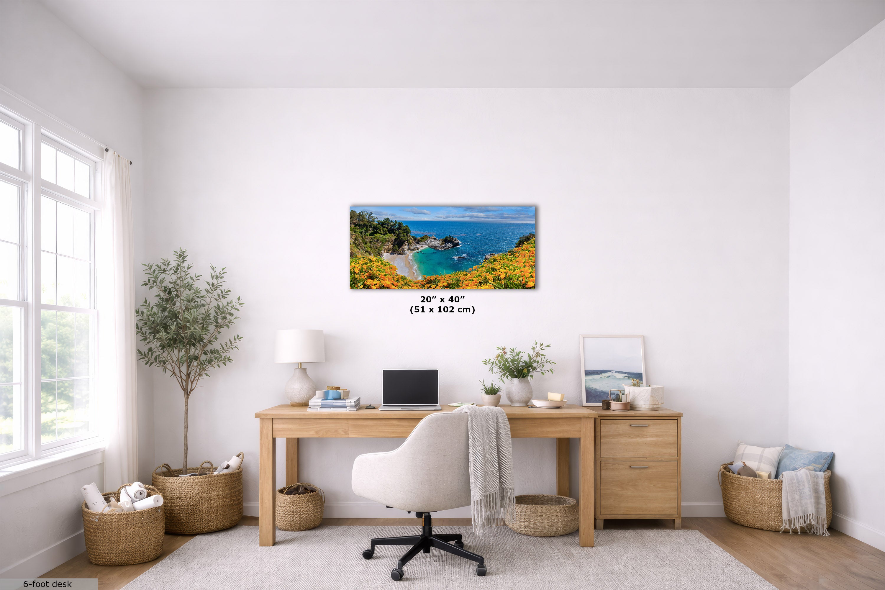 A horizontal canvas print of a coastal landscape with blue water, green cliffs, and yellow wildflowers, displayed on a white wall above a wooden desk in a bright, modern home office. The text '20" x 40" (51 x 102 cm)' is overlaid in the center of the canvas.