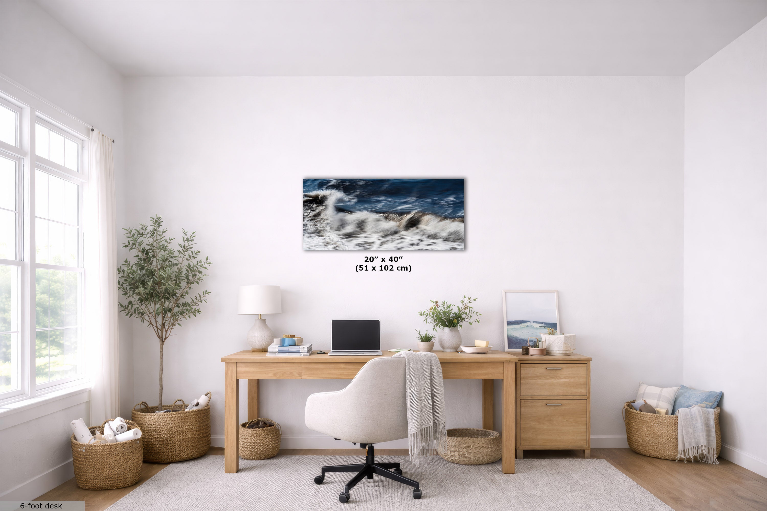 A rectangular wall art print showing a blue ocean wave scene, displayed in a bright, modern home office above a wooden desk. The room features a white swivel chair, a lamp, plants, and woven baskets.