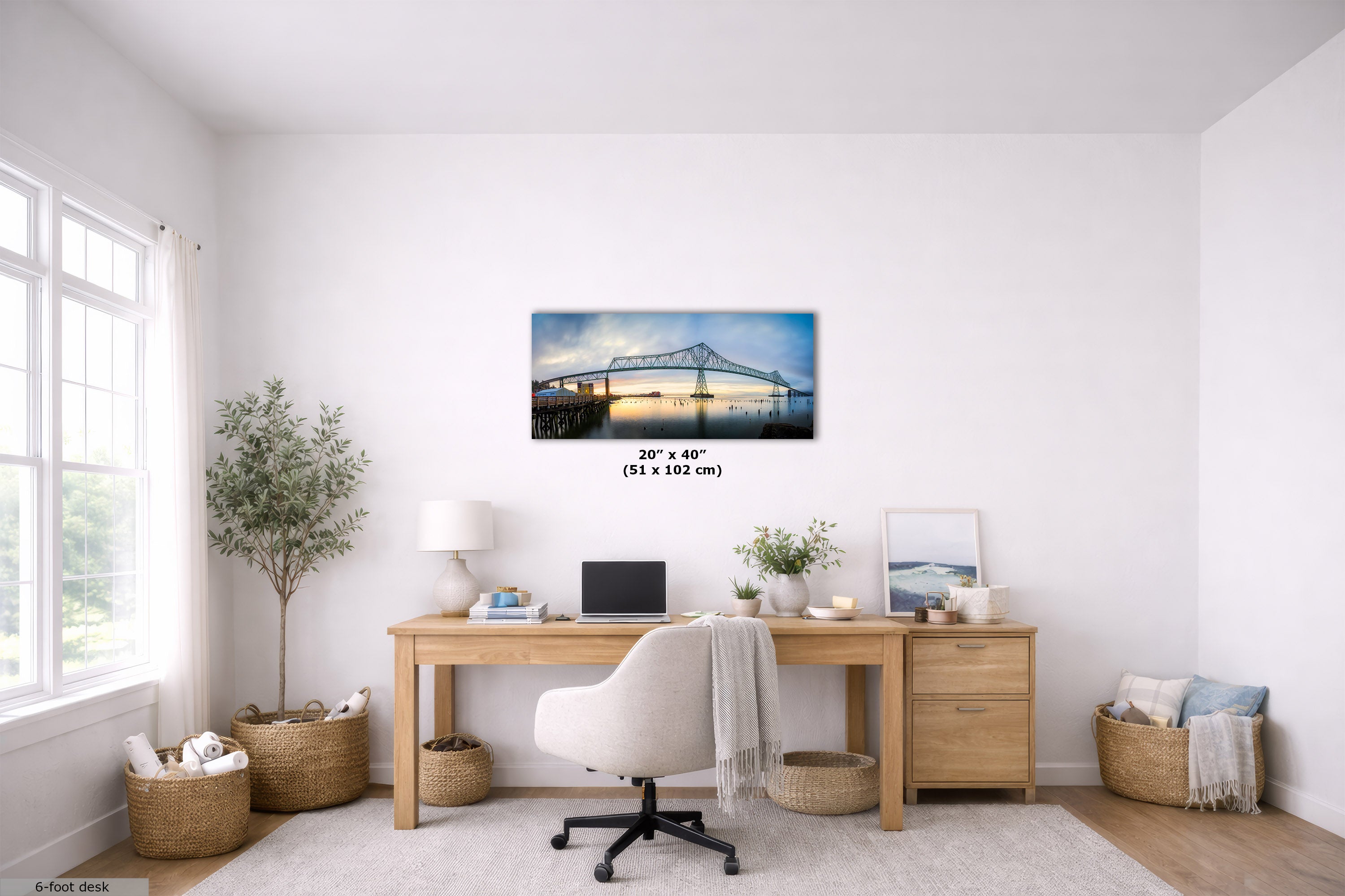 A framed wall art print depicting a bridge over water, displayed in a bright, modern home office setting above a wooden desk. The print has a visible size overlay indicating 20 x 40 inches (51 x 102 cm).