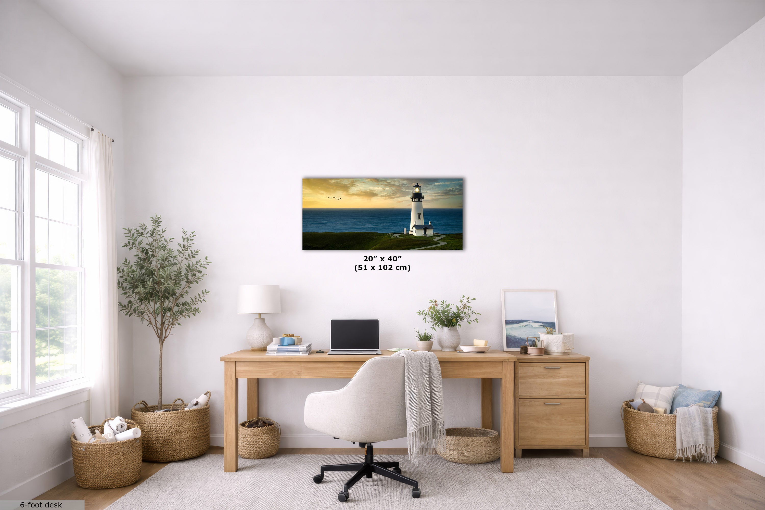 A framed wall art print depicting a lighthouse by the ocean, shown hanging above a wooden desk in a bright, modern home office. The print has a black border and size text in the center reading 20 x 40 (51 x 102 cm).
