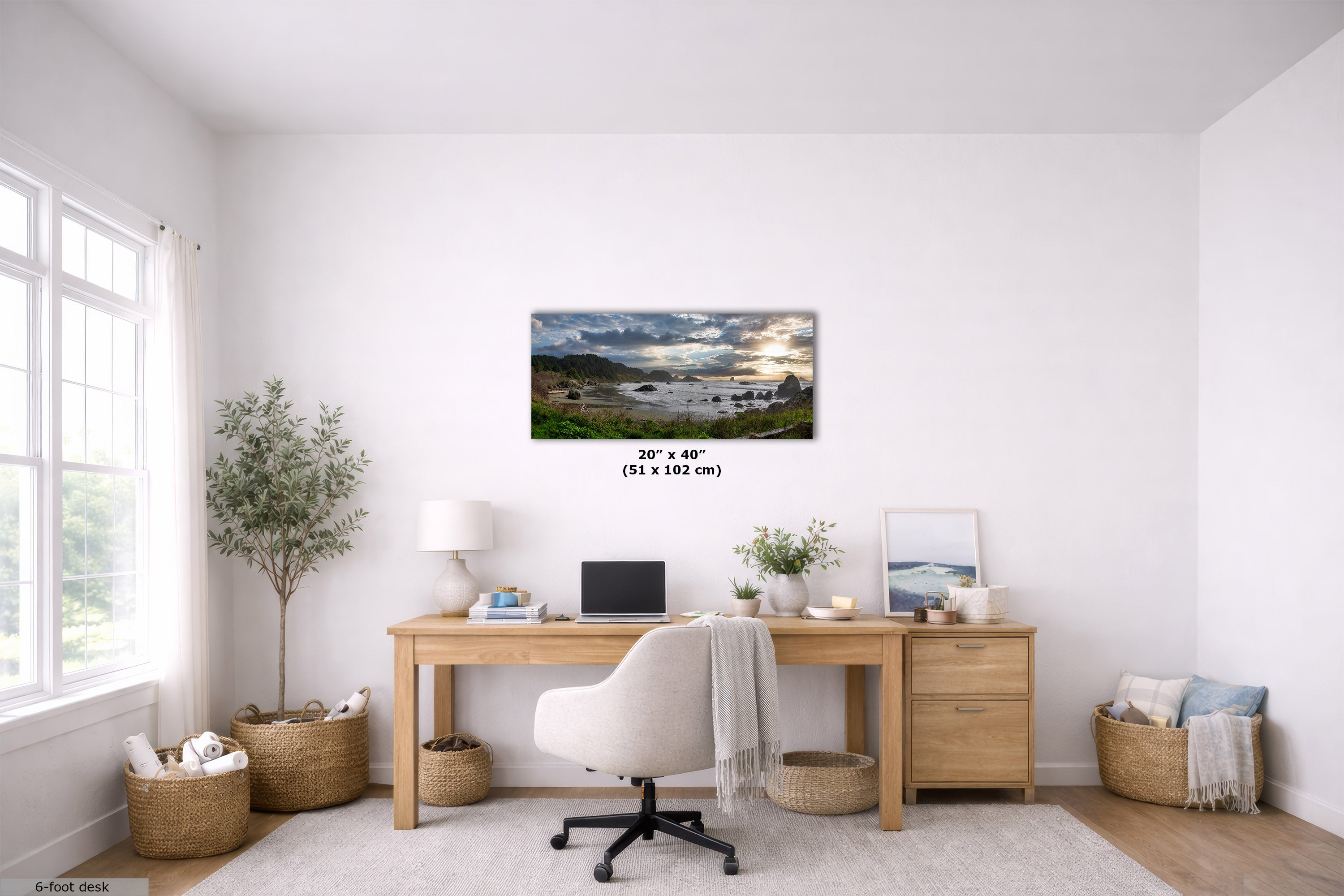 A framed landscape art print depicting a scenic lake and mountains under a cloudy sky, displayed on a white wall in a modern, bright home office setting above a wooden desk.