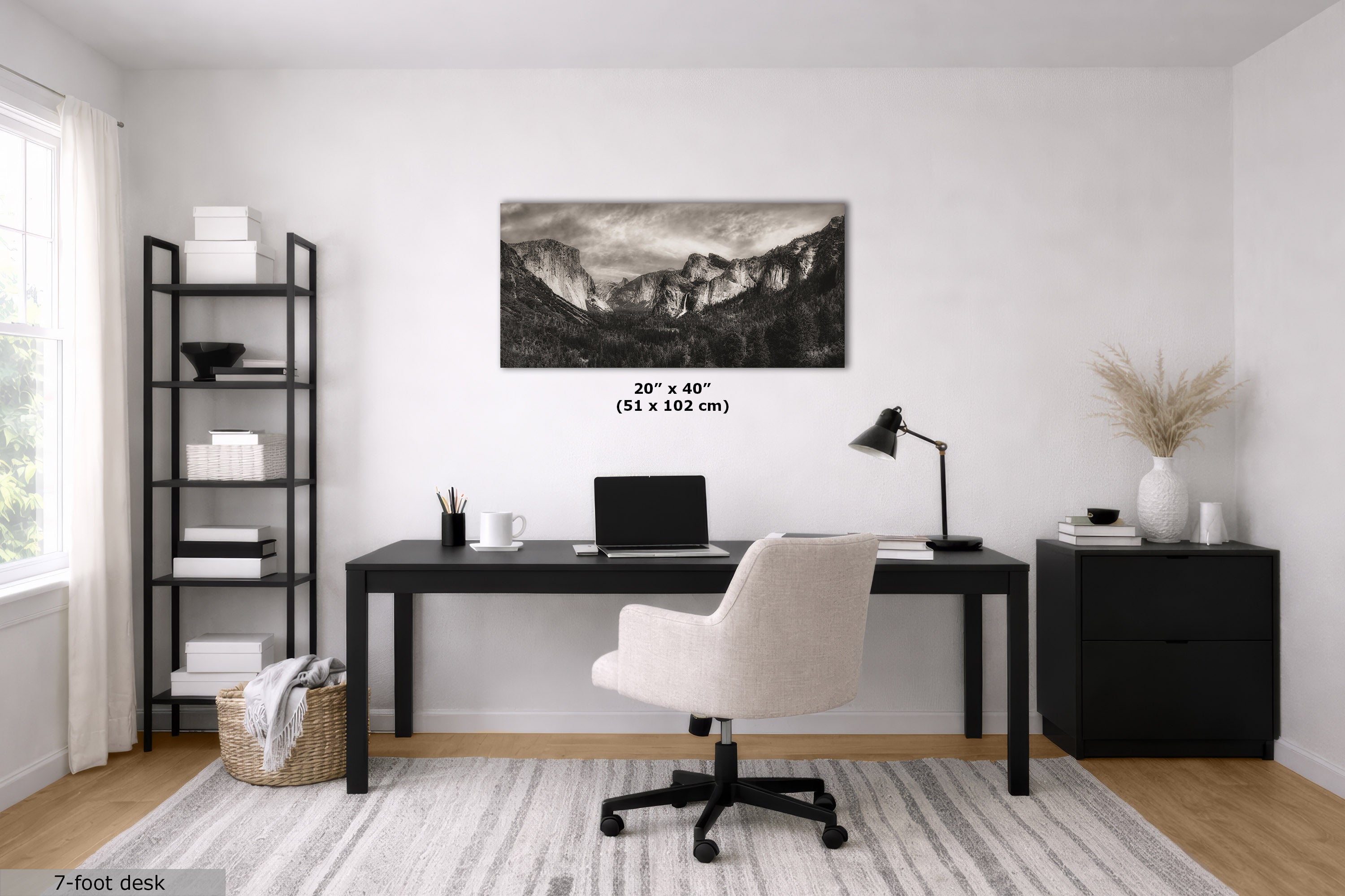 A black and white mountain landscape wall art print displayed in a modern home office setting above a black desk and white swivel chair, with size text '20" x 40" (51 x 102 cm)' printed directly on the image.