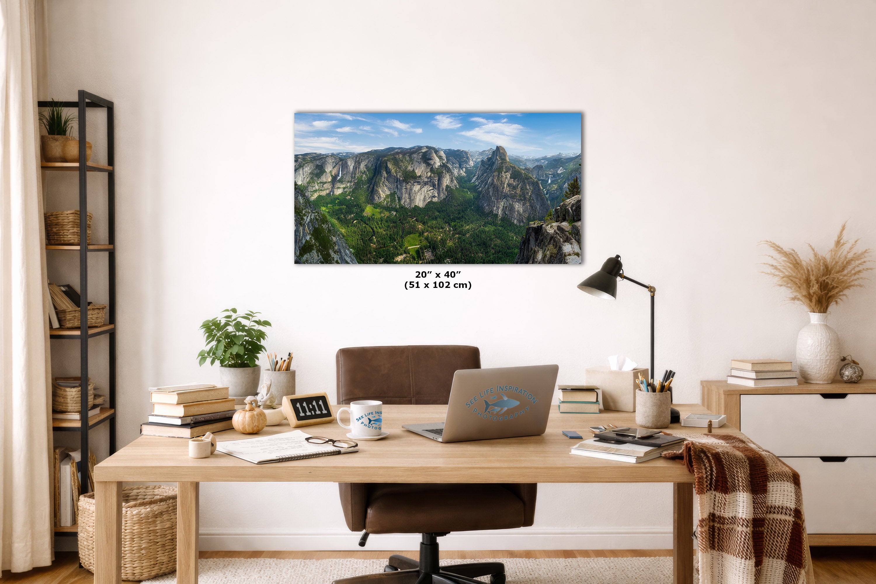 A wall art print showing a mountain landscape with green valleys and blue sky, displayed above a wooden desk in a styled home office. The print includes size text reading 20" x 40" (51 x 102 cm).