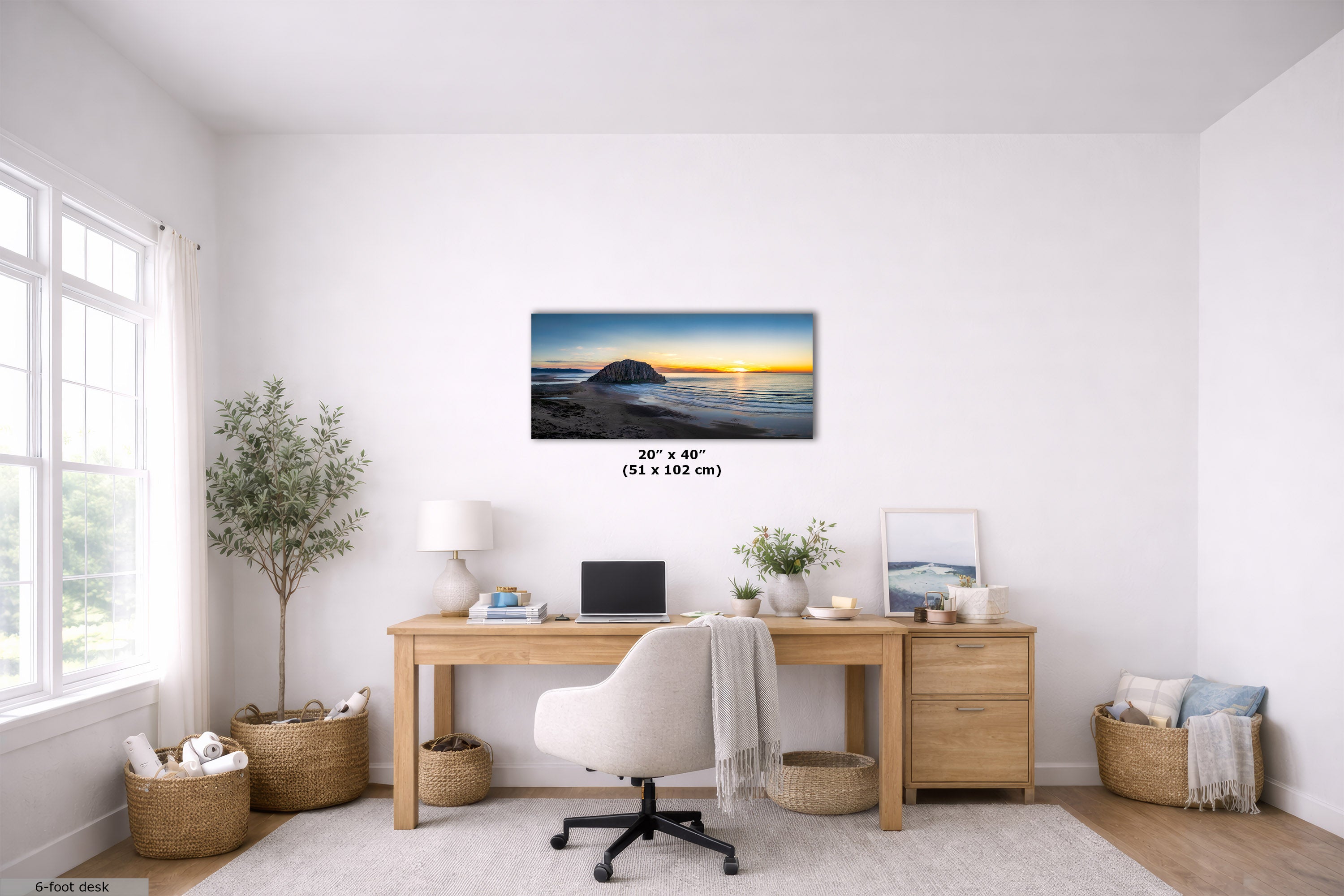 A horizontal canvas wall art print depicting a sunset over ocean waves, displayed in a modern, bright home office setting above a wooden desk. The print features a black frame and includes size text indicating 20 x 40 inches (51 x 102 cm).