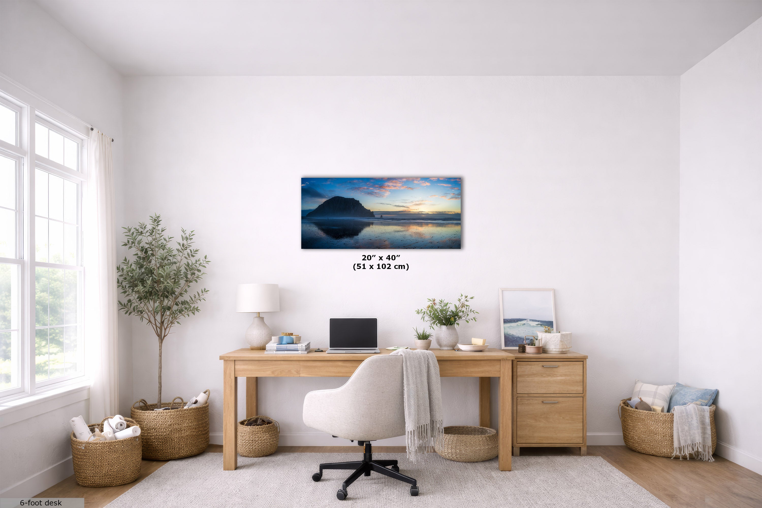 A panoramic landscape art print of a mountain lake at sunset is displayed on a white wall in a modern, bright home office setting with a wooden desk, white chair, and plants.