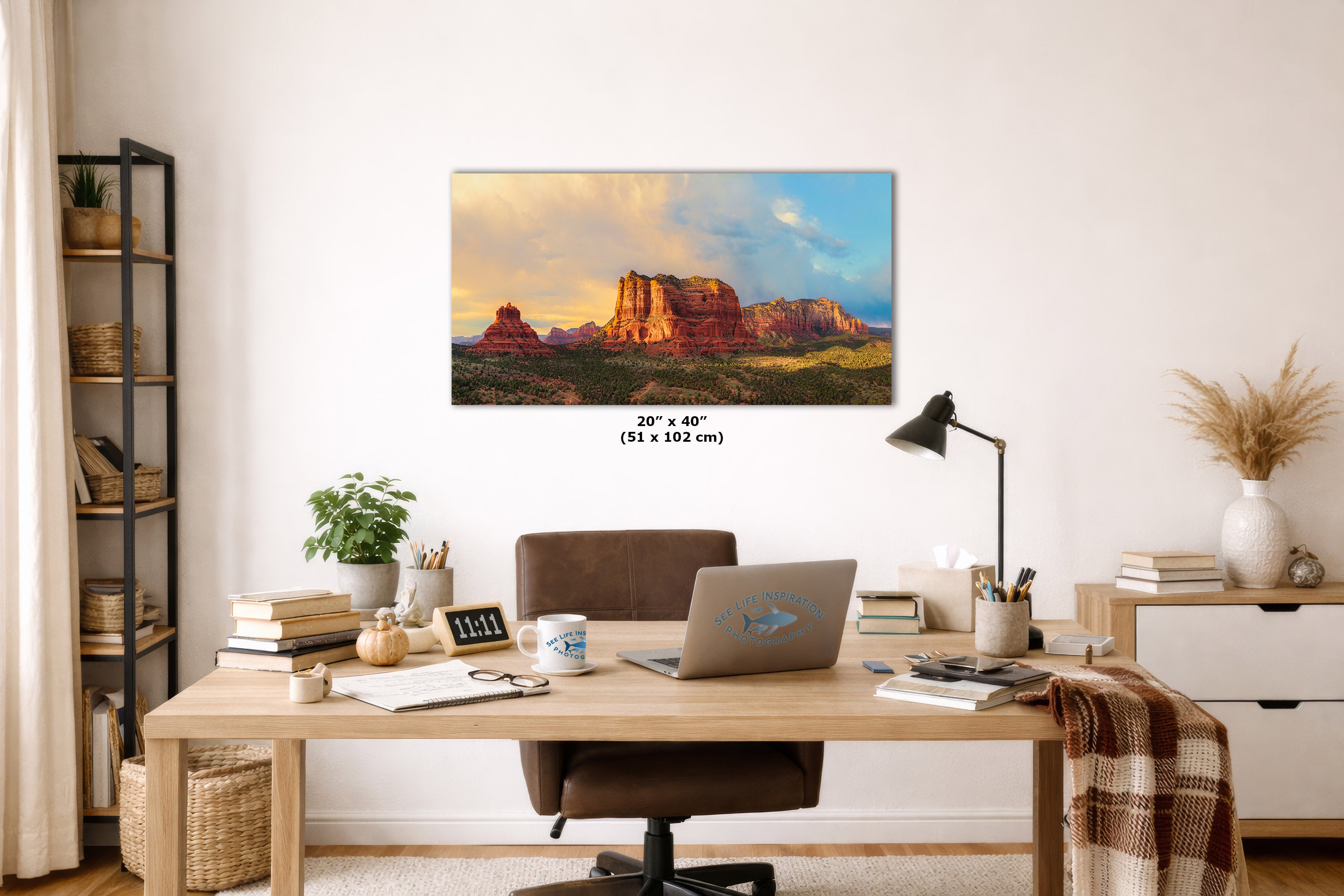 A framed wall art print showing a desert rock landscape at sunset hangs above a wooden desk in a styled home office. The print includes size text reading 20 x 40 inches (51 x 102 cm).