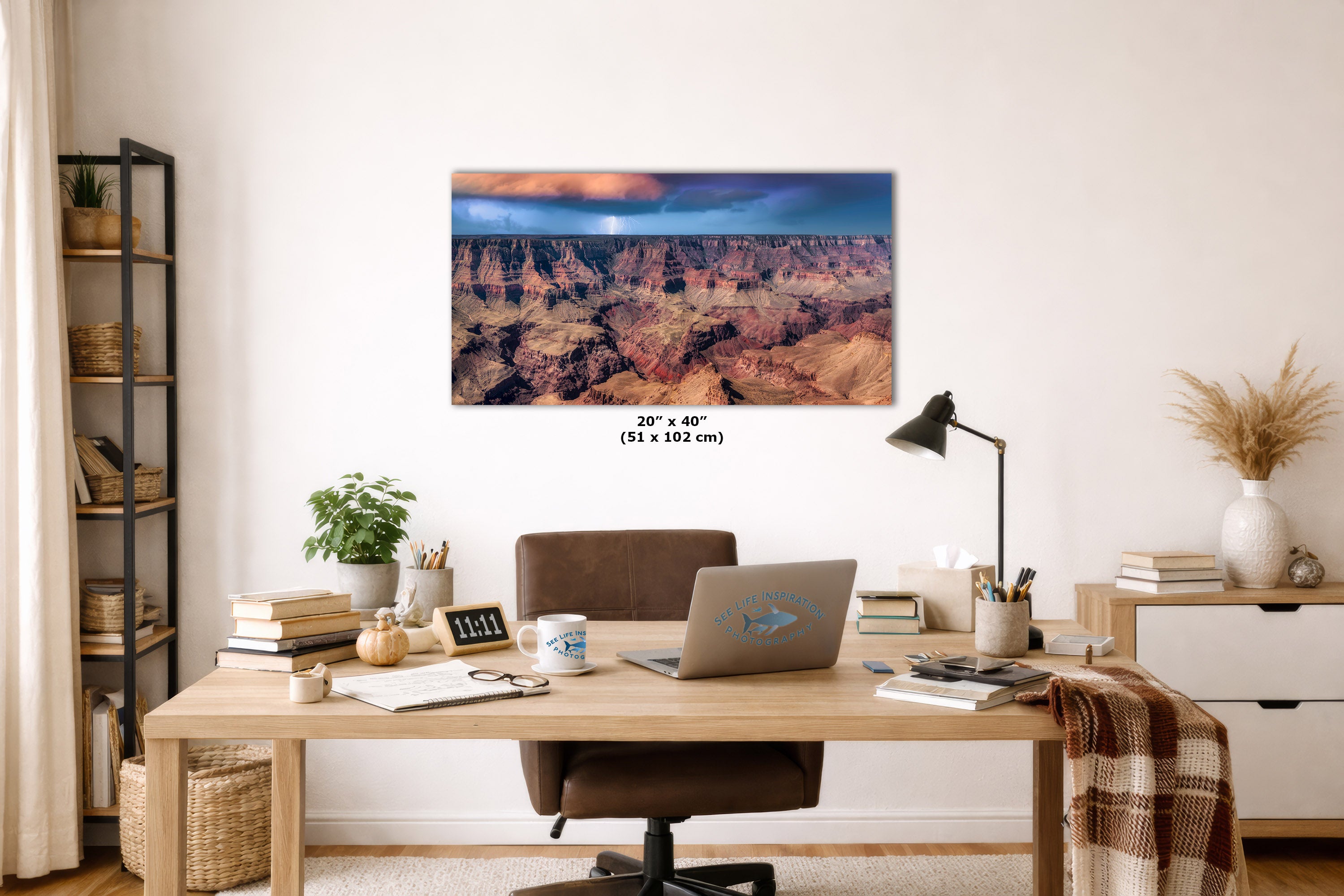 A wall art print showing a canyon landscape with a blue sky, displayed above a wooden desk in a styled home office. The print includes size text reading 20" x 40" (51 x 102 cm).