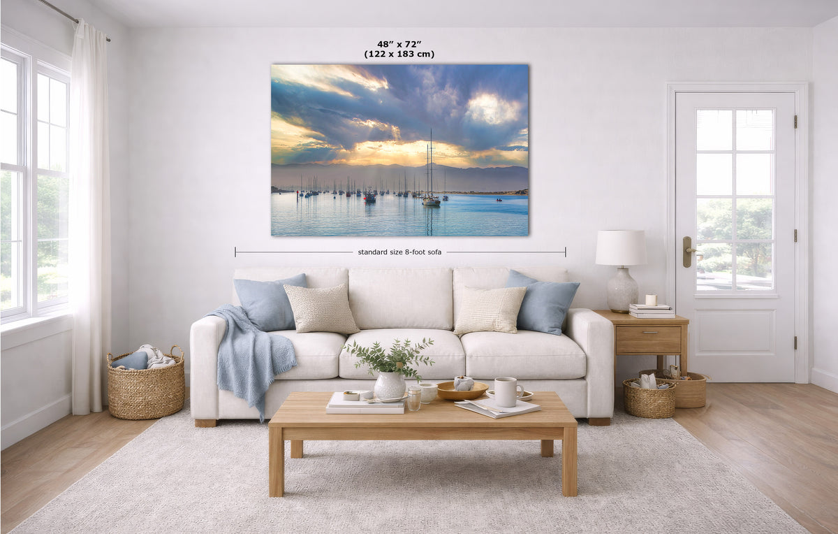 A large wall art print showing a harbor sunrise with sailboats, displayed above a white sofa in a bright living room. Black measurement lines and text indicate the print size as 48 x 72 inches (122 x 183 cm).